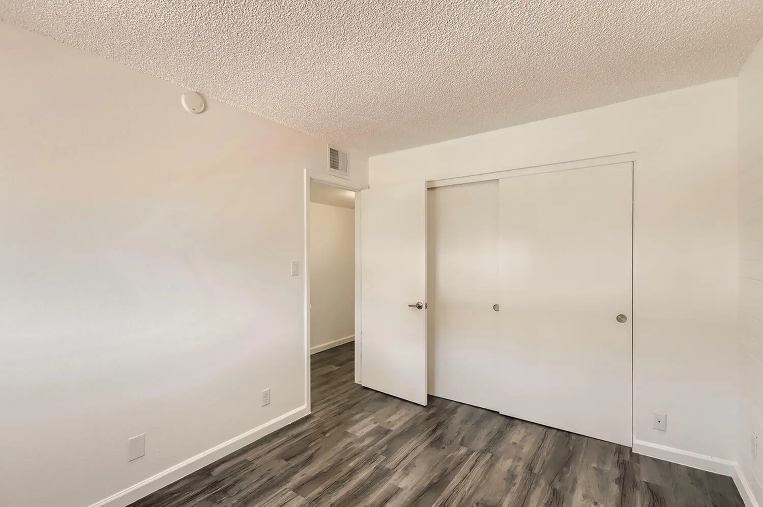 Bedroom, wood-style plank flooring, white walls, sliding closet doors, entry door