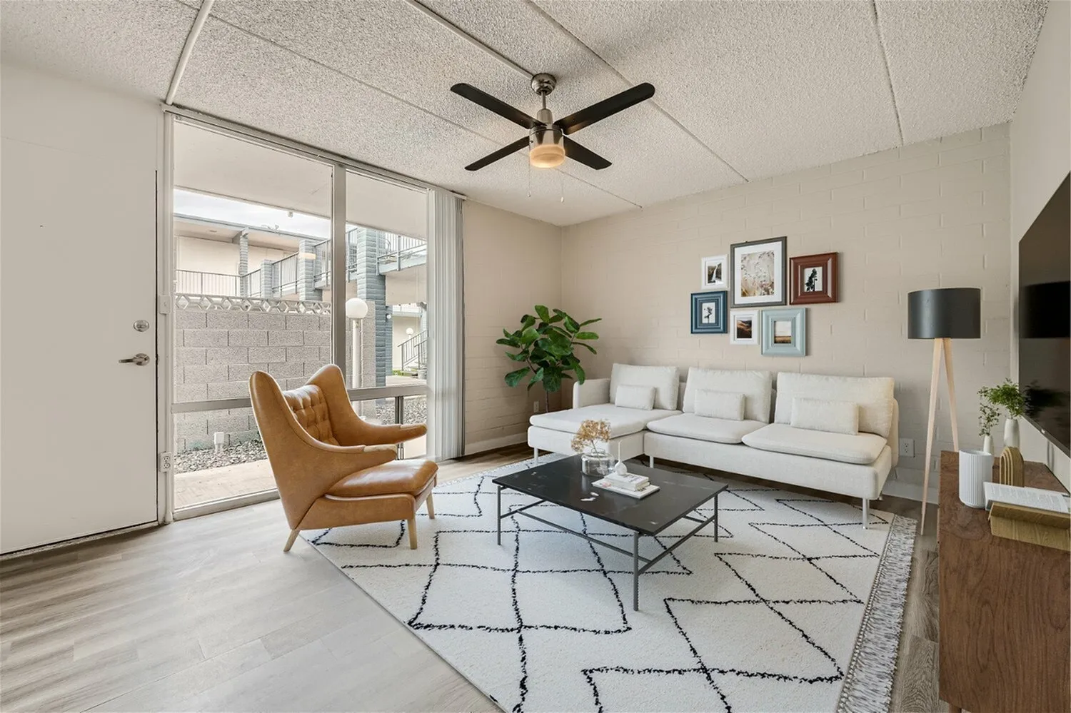 Living room, wood-style plank flooring, ceiling fan, white sofa, caramel leather chair