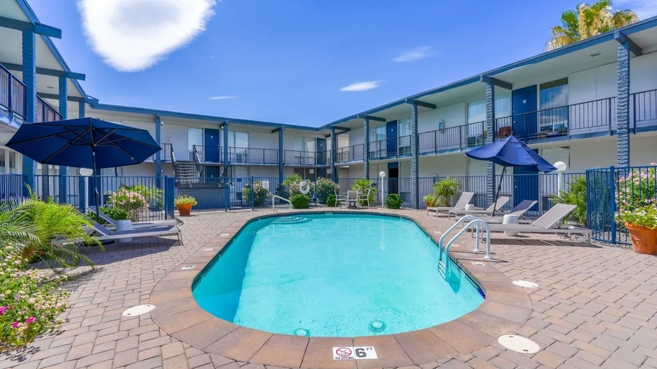 Resort-style pool, blue umbrellas, loungers, brick patio, multi-unit building
