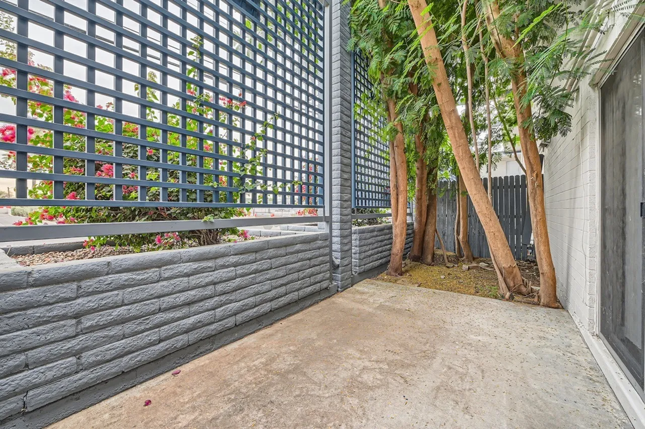 Courtyard with concrete patio, horizontal gray fence, green lattice screens, mature trees