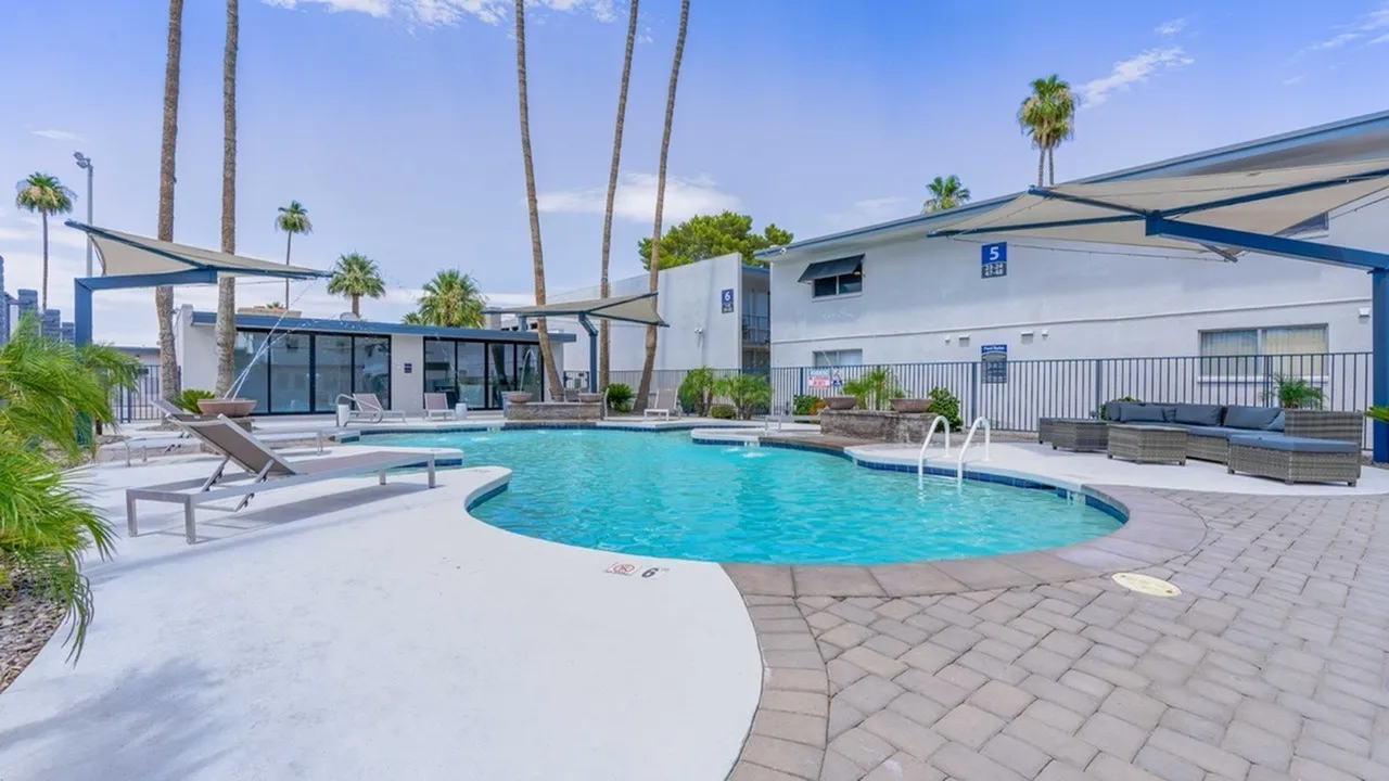 Resort-style pool, curved lounge seating, blue sun shades, palm trees, Phoenix