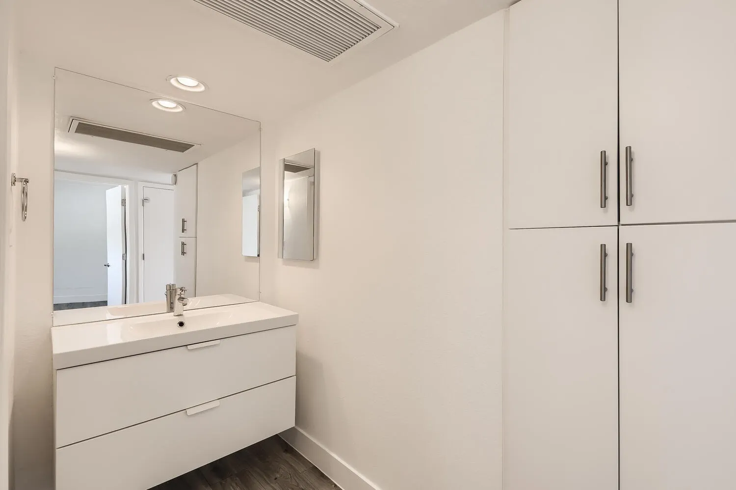 Primary bathroom, white floating vanity, quartz countertop, large mirror, chrome fixtures, wood-style plank flooring