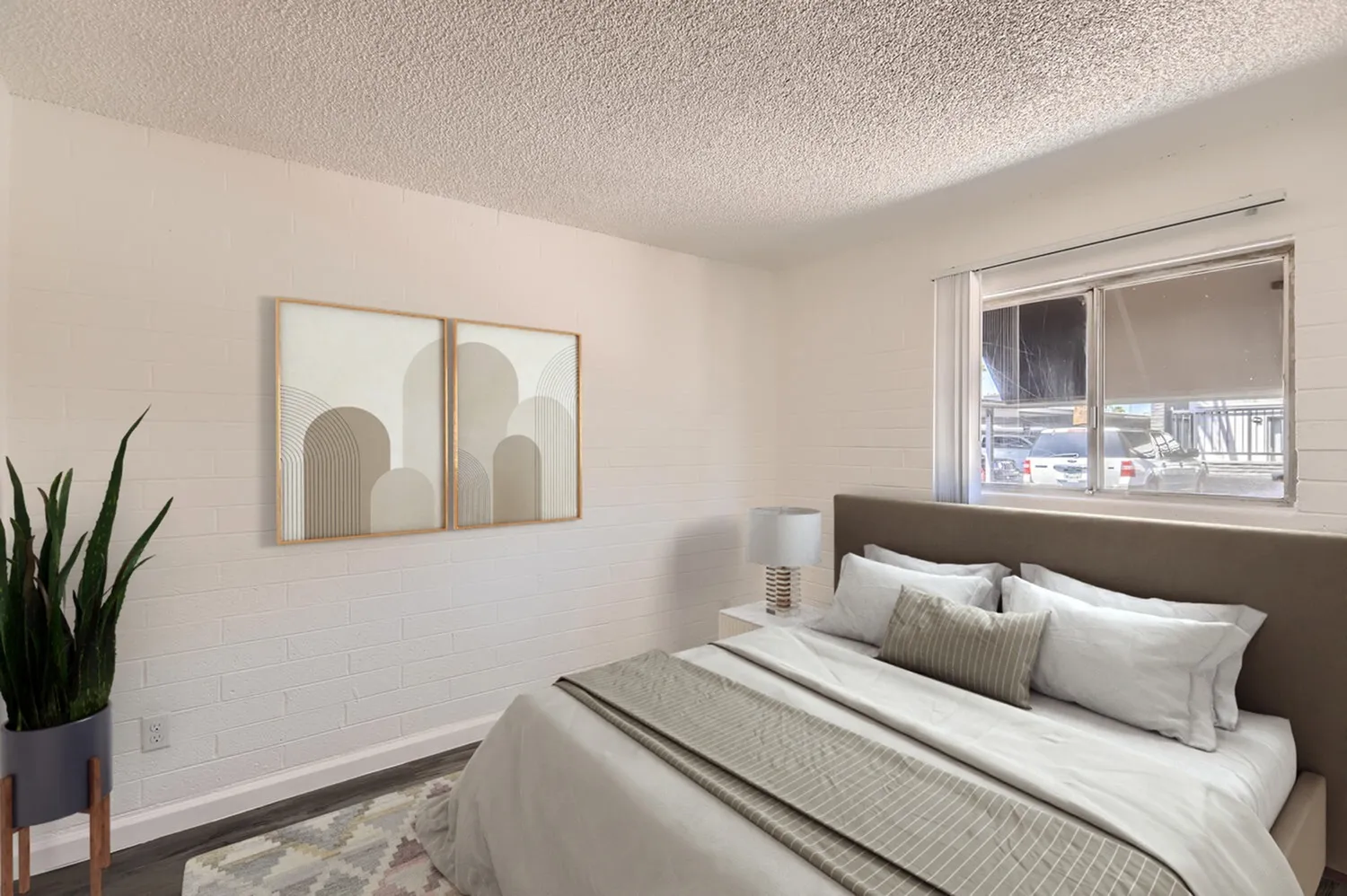 Primary bedroom, gray upholstered headboard, white bedding, framed abstract wall art, potted plant, large window with blinds