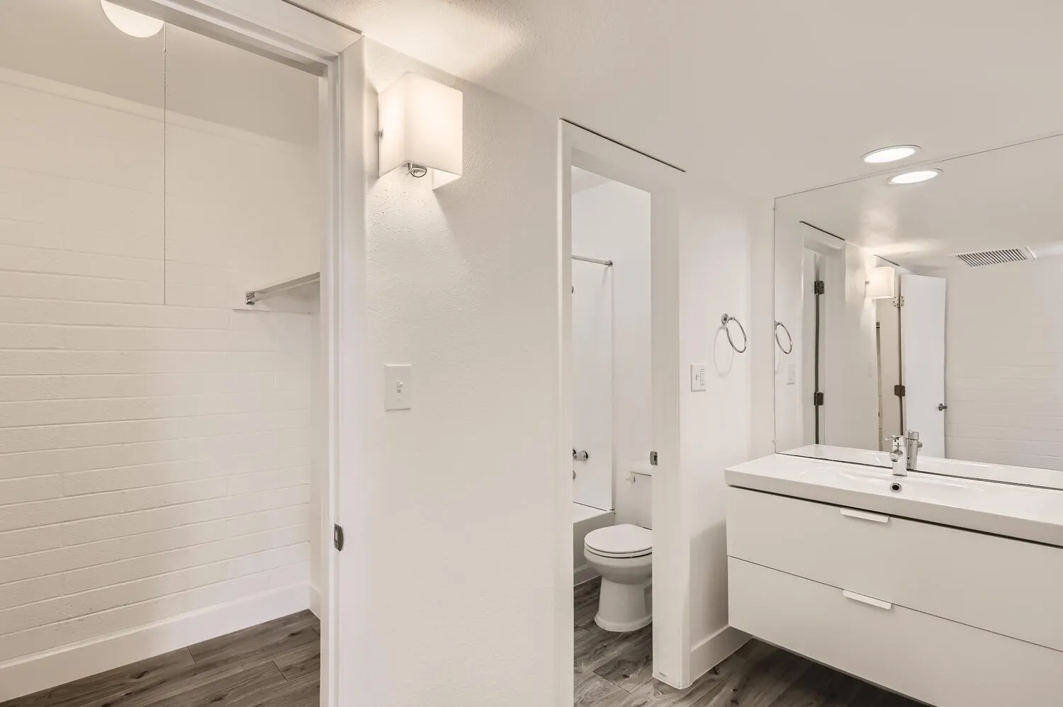 Primary bathroom, white subway tile shower surround, floating vanity with quartz countertop, wood-style plank flooring