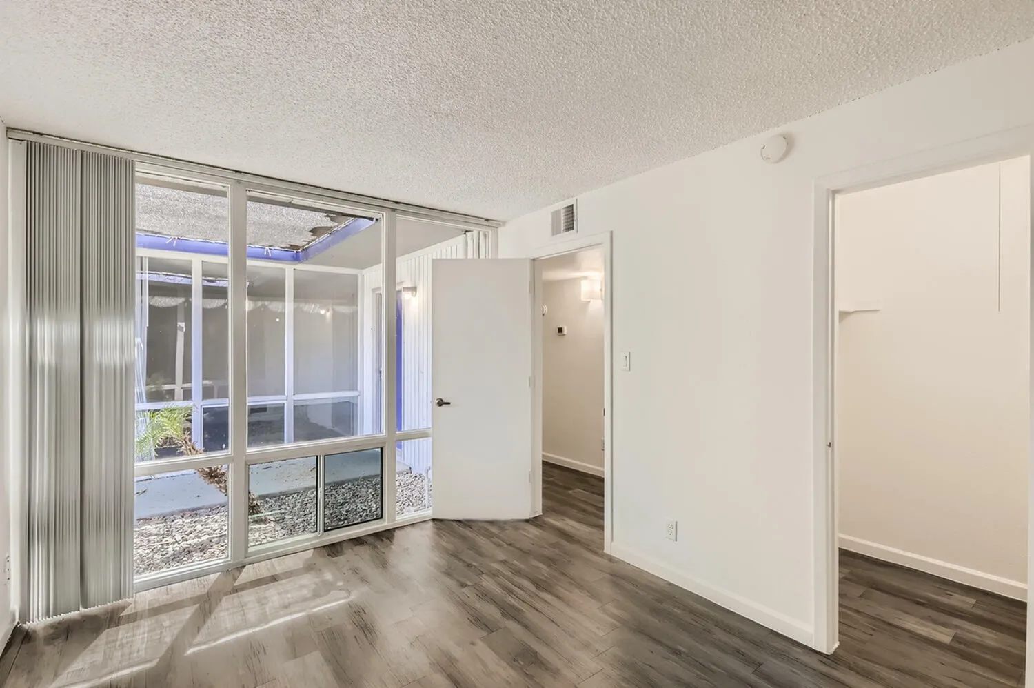 Living room, wood-style plank flooring, glass sliding doors, vertical blinds, open layout