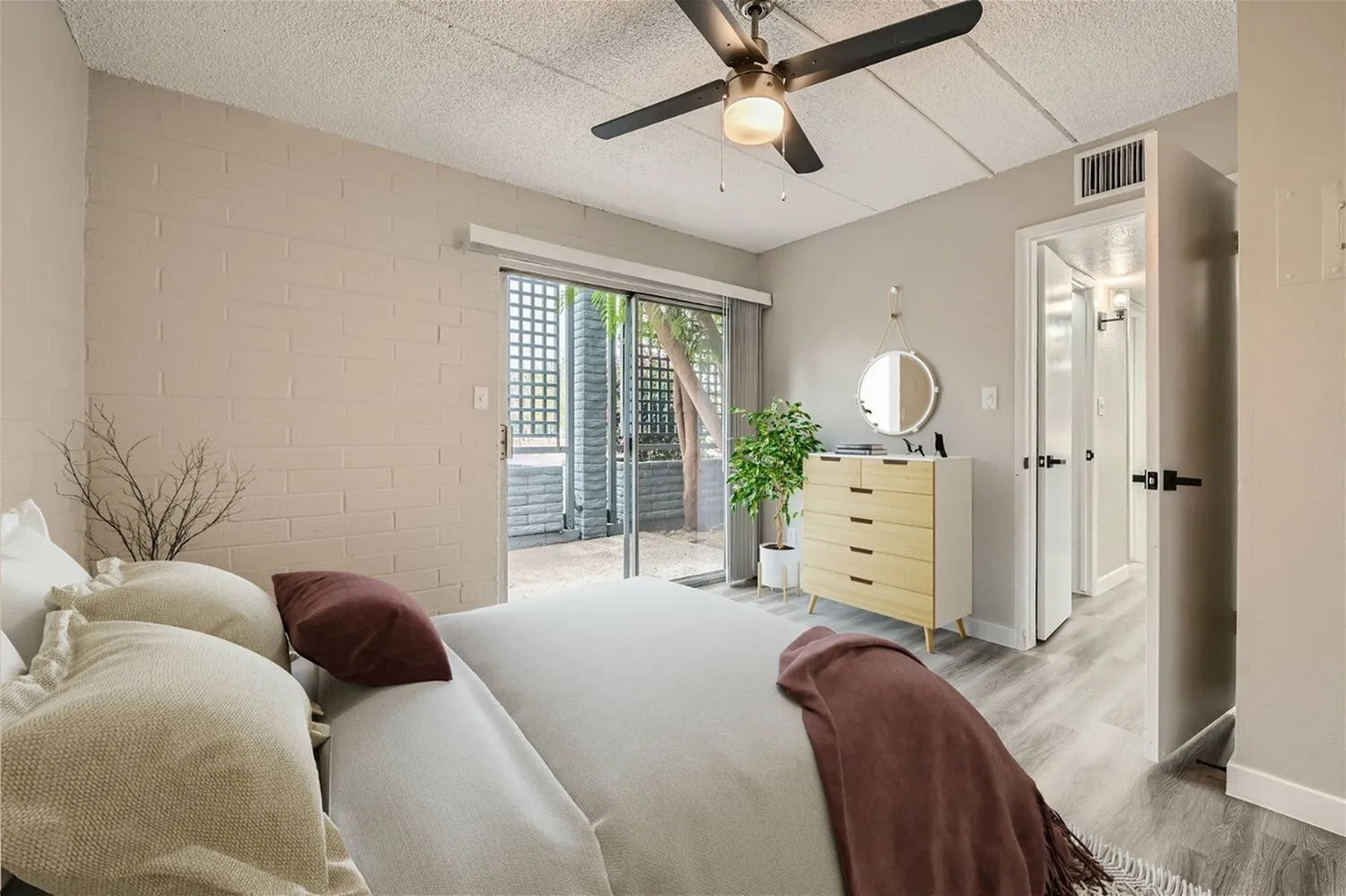 Primary bedroom, wood-style plank flooring, ceiling fan, patio doors, yellow dresser