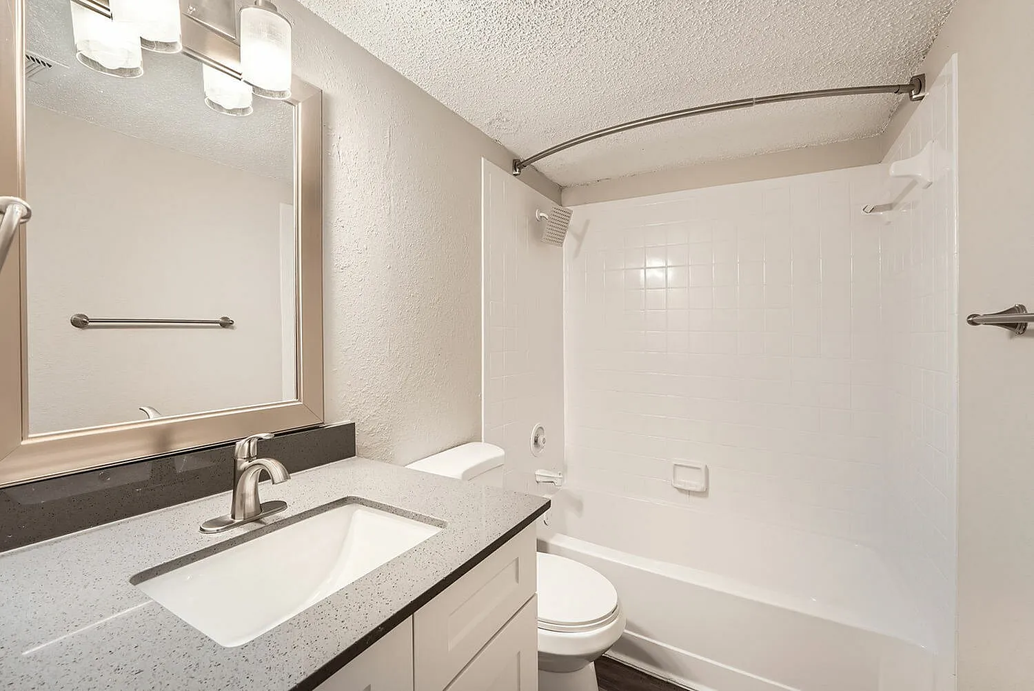 Primary bathroom, quartz countertops, white cabinetry, framed mirror, white tile surround shower