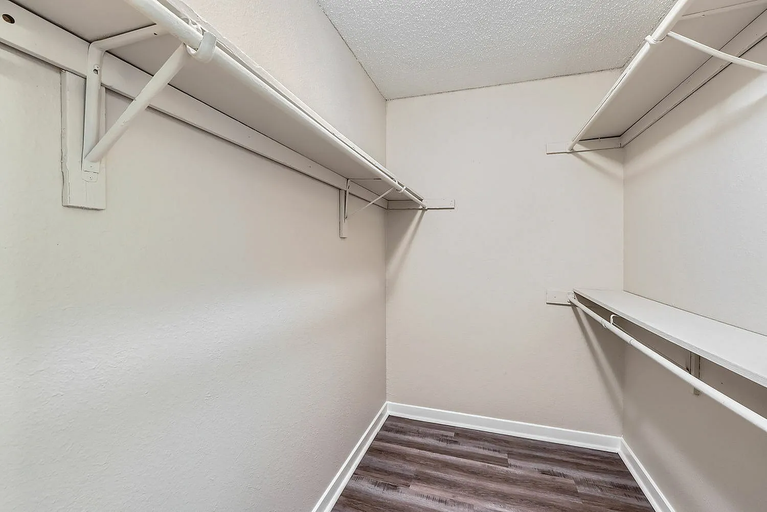 Walk-in closet, white painted walls, metal hanging rods, wood-style plank flooring