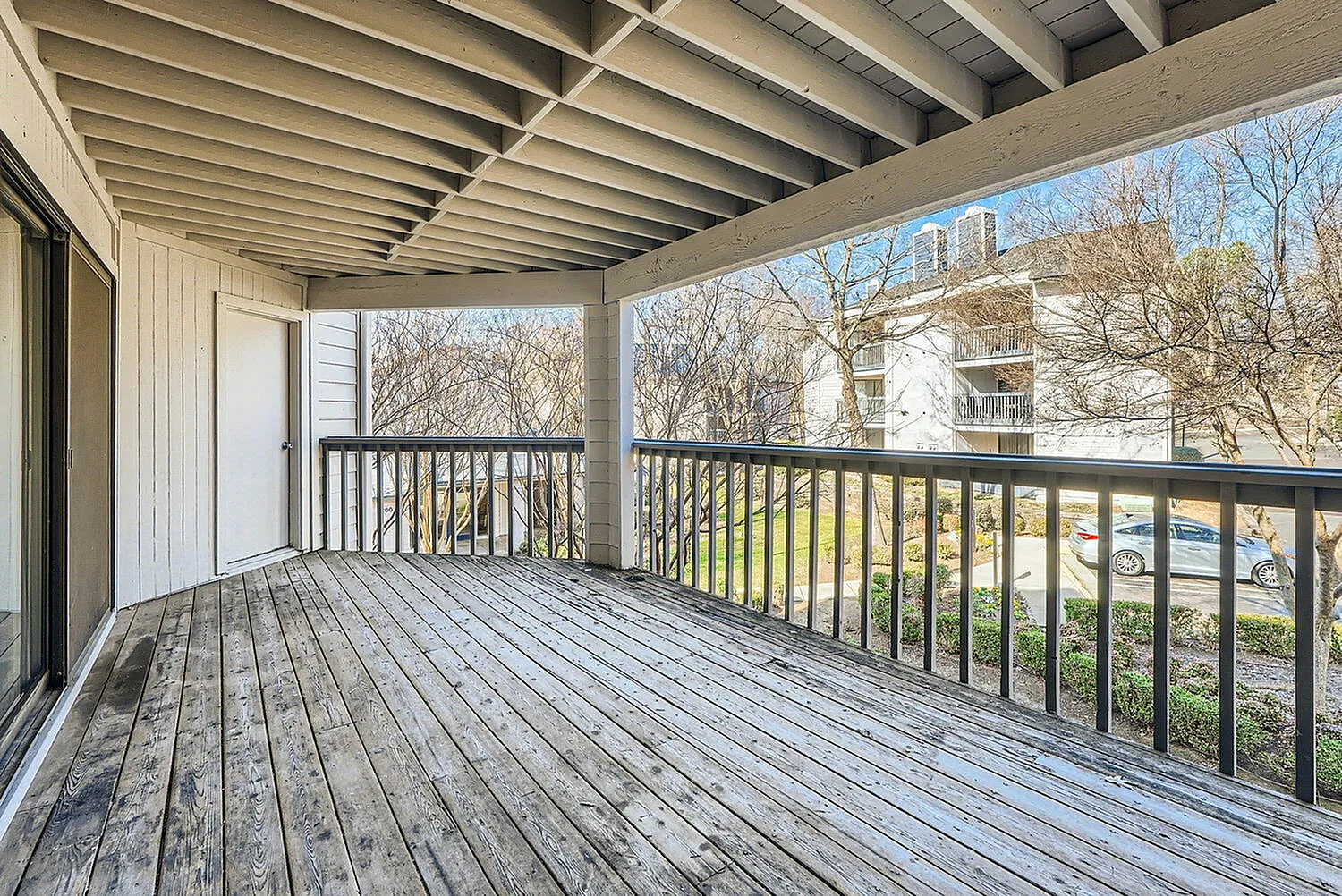 Covered deck, wood-style plank flooring, black railing, exposed beam ceiling