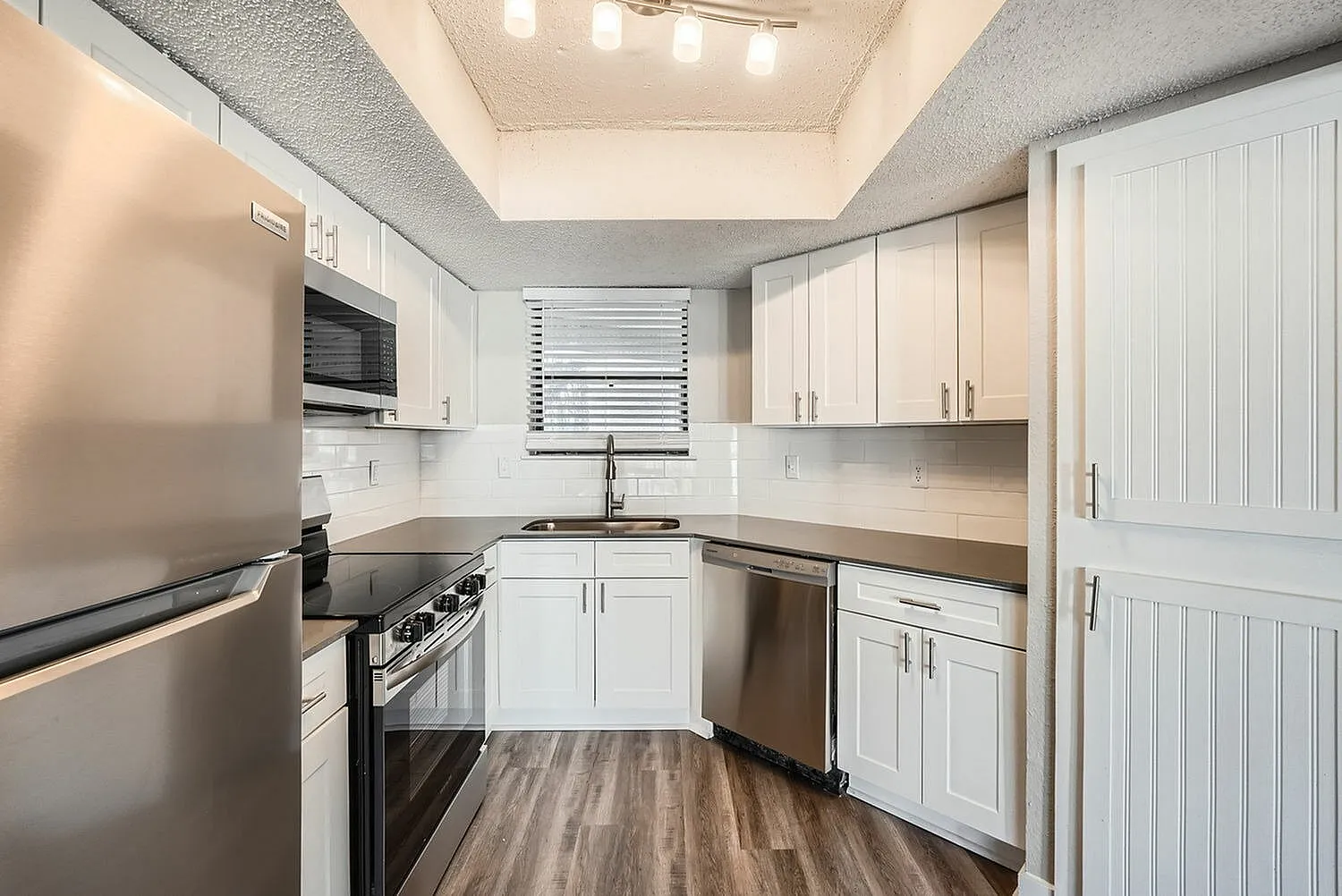 Kitchen, white shaker cabinetry, stainless steel appliances, wood-style plank flooring, quartz countertops
