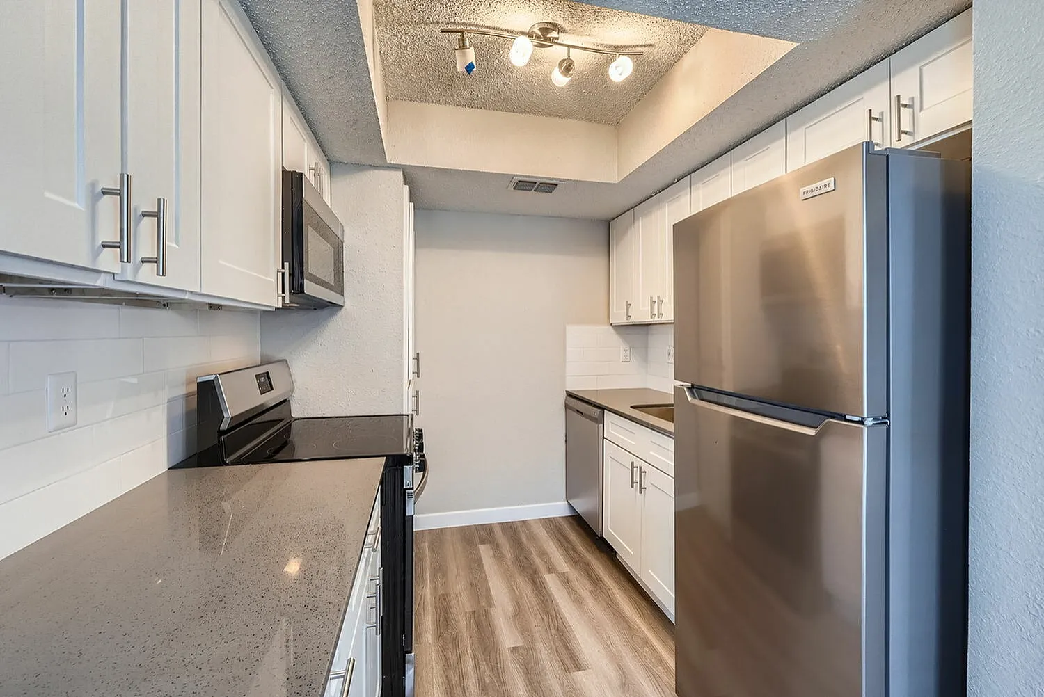 Kitchen, white shaker cabinetry, gray quartz countertops, stainless steel appliances, wood-style plank flooring
