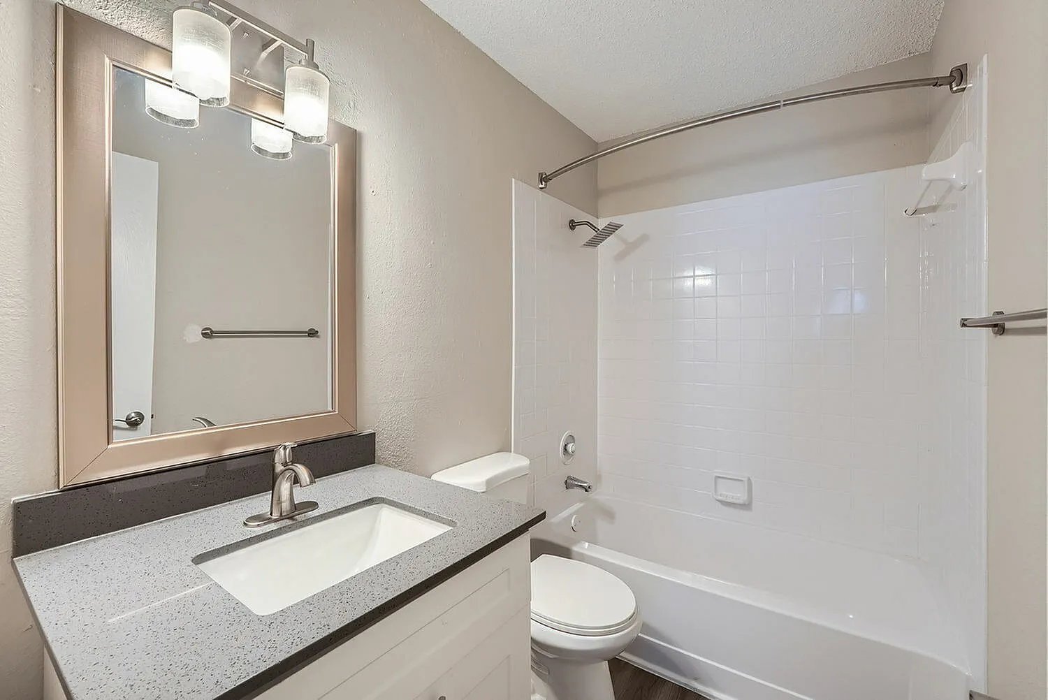 Primary bathroom, gray quartz countertops, framed mirror with lighting, tile shower enclosure
