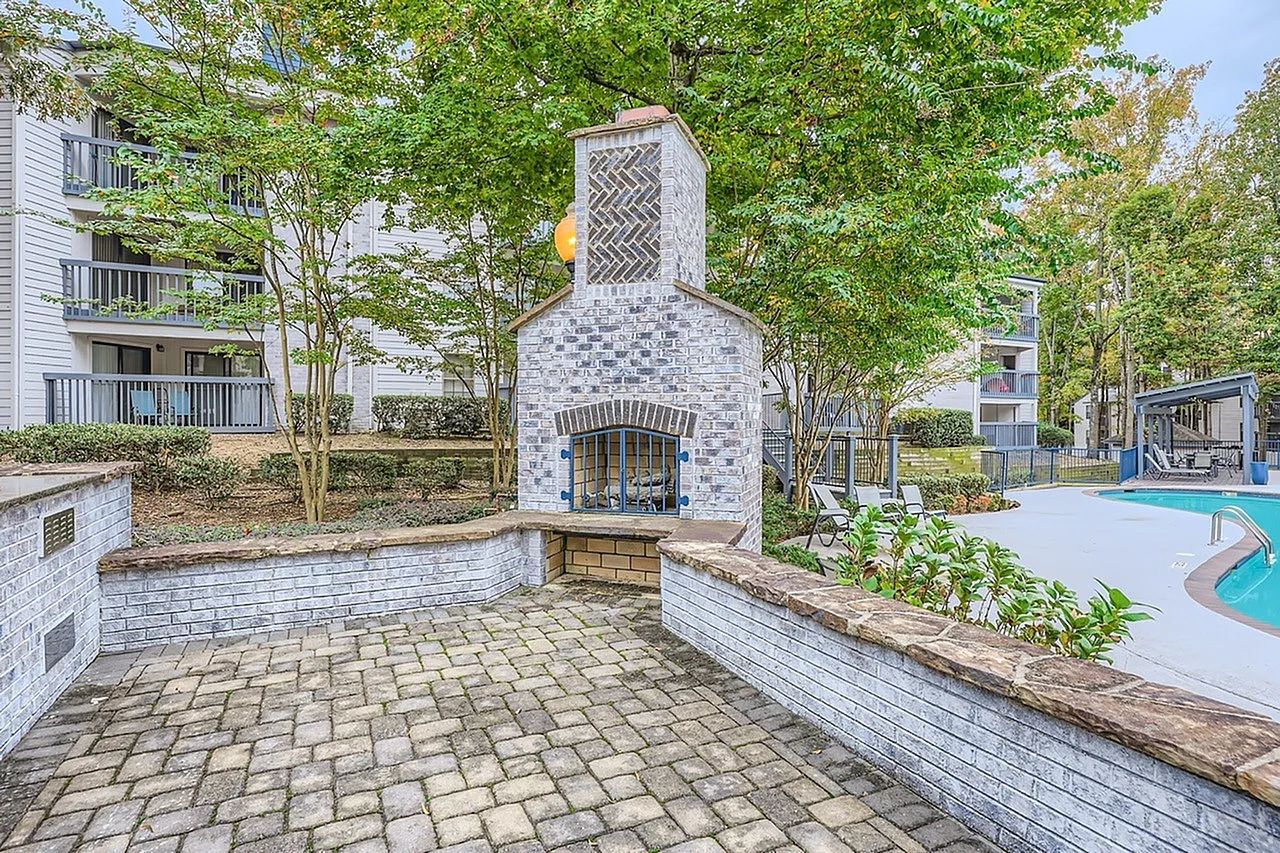 Outdoor patio area, tile fireplace with arched opening, paver flooring, wood seating walls, trees, pool area