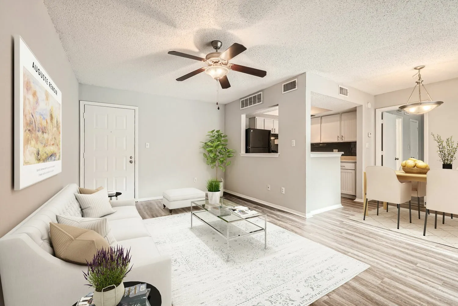 Living room with wood-style plank flooring, ceiling fan, white sofa, glass coffee table, kitchen with black cabinetry