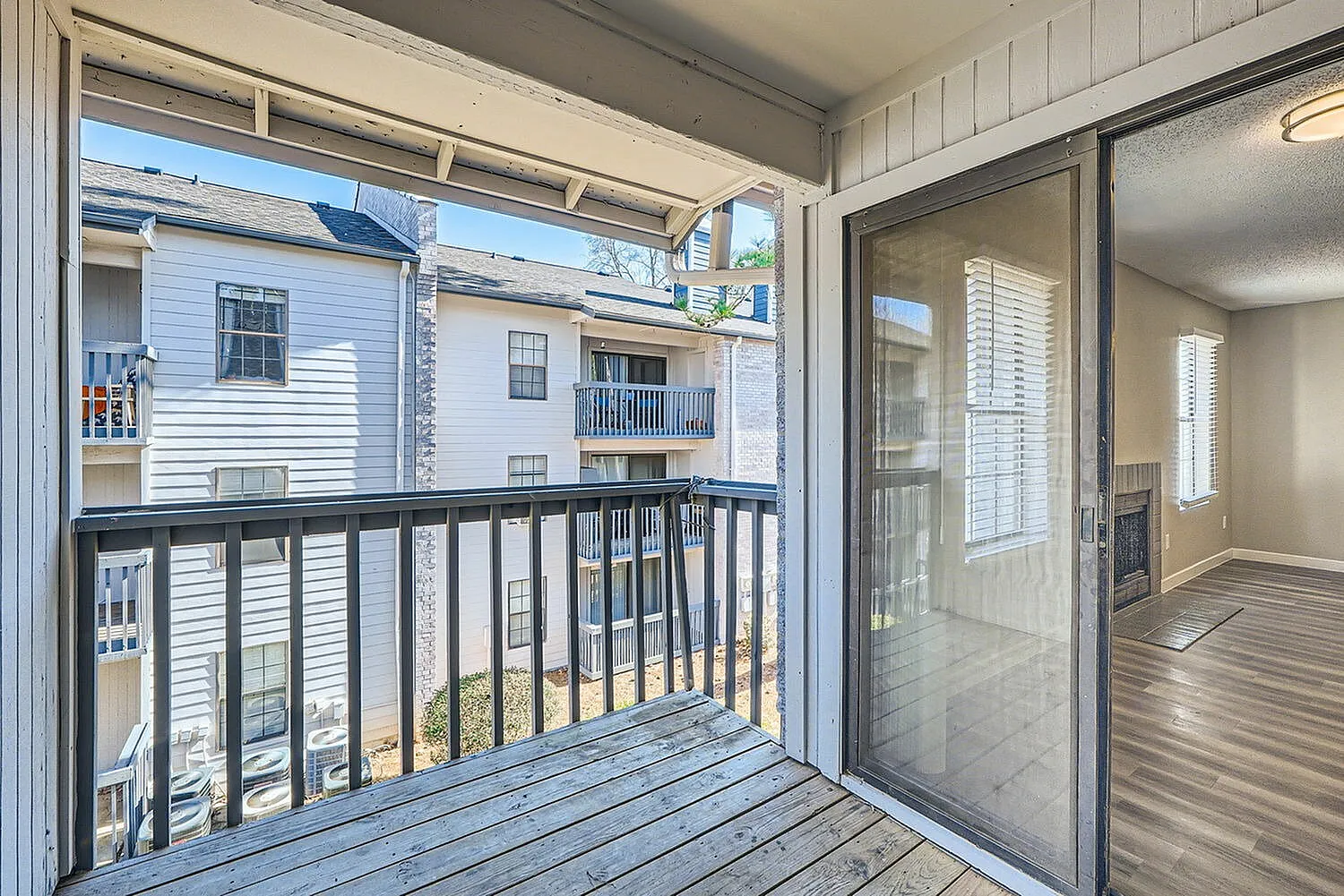 Balcony, black railing, wood-style plank flooring, sliding glass door, neighboring buildings