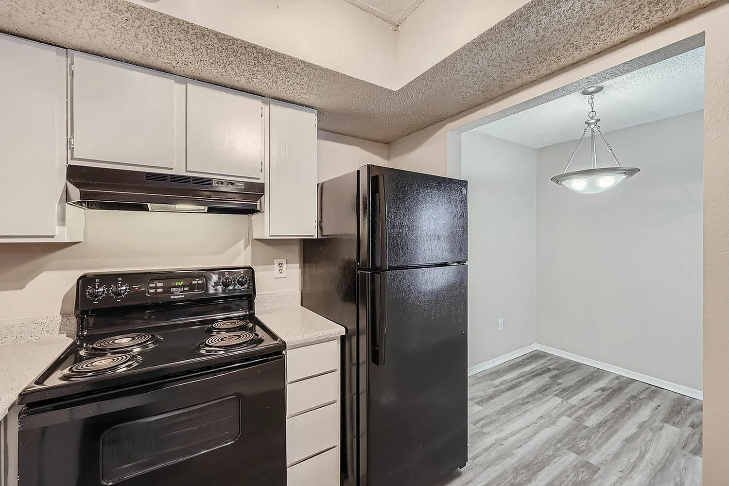 Kitchen, black electric range, black top-freezer refrigerator, white cabinetry, wood-style plank flooring