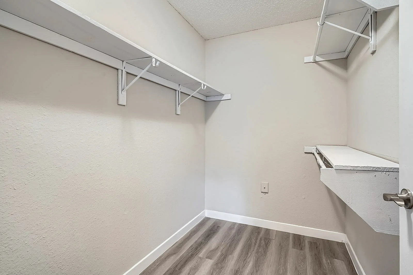 Walk-in closet, metal shelving, wood-style plank flooring, white walls, hanging rod