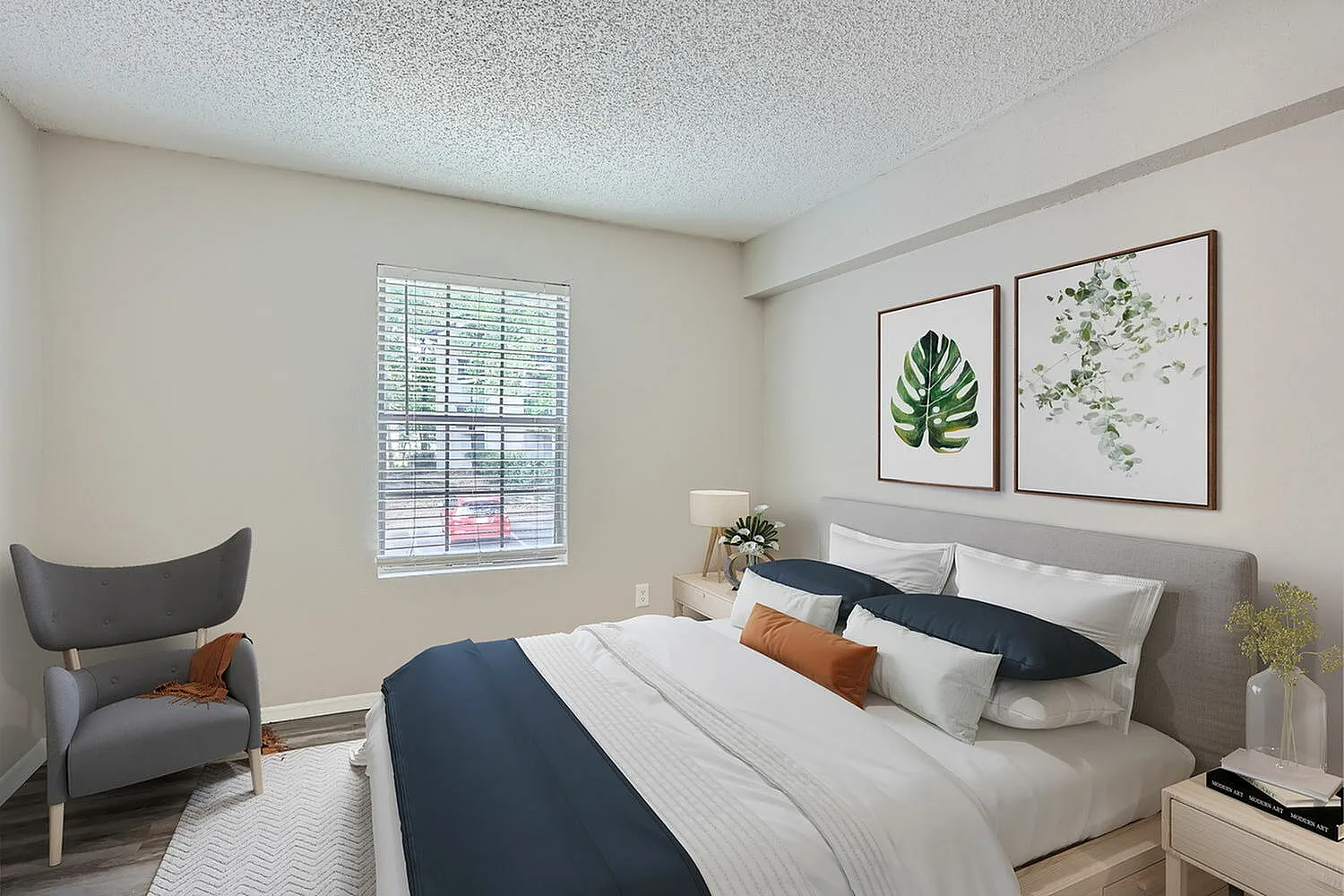 Primary bedroom, gray upholstered headboard, navy and white bedding, botanical wall art, gray accent chair