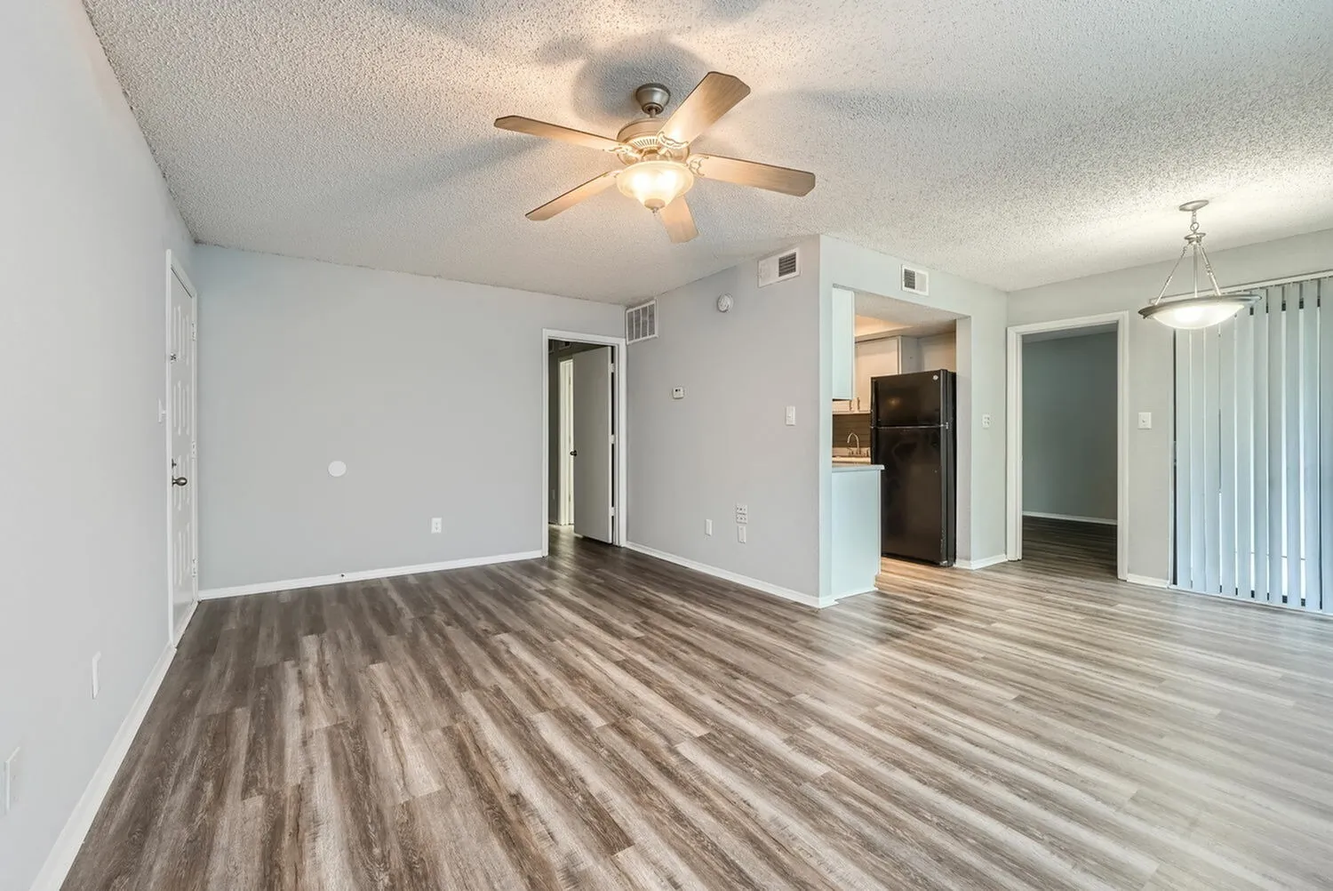 Living room, wood-style plank flooring, ceiling fan, white walls, entry to kitchen