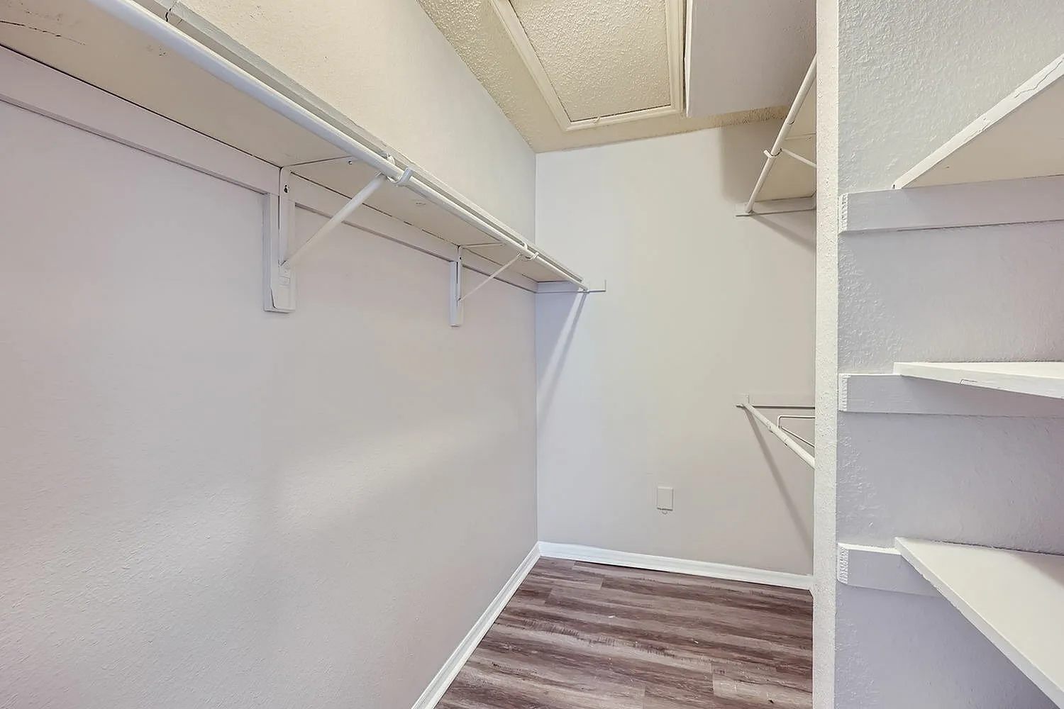 Walk-in closet, white walls, wooden clothing rod, shelving, wood-style plank flooring