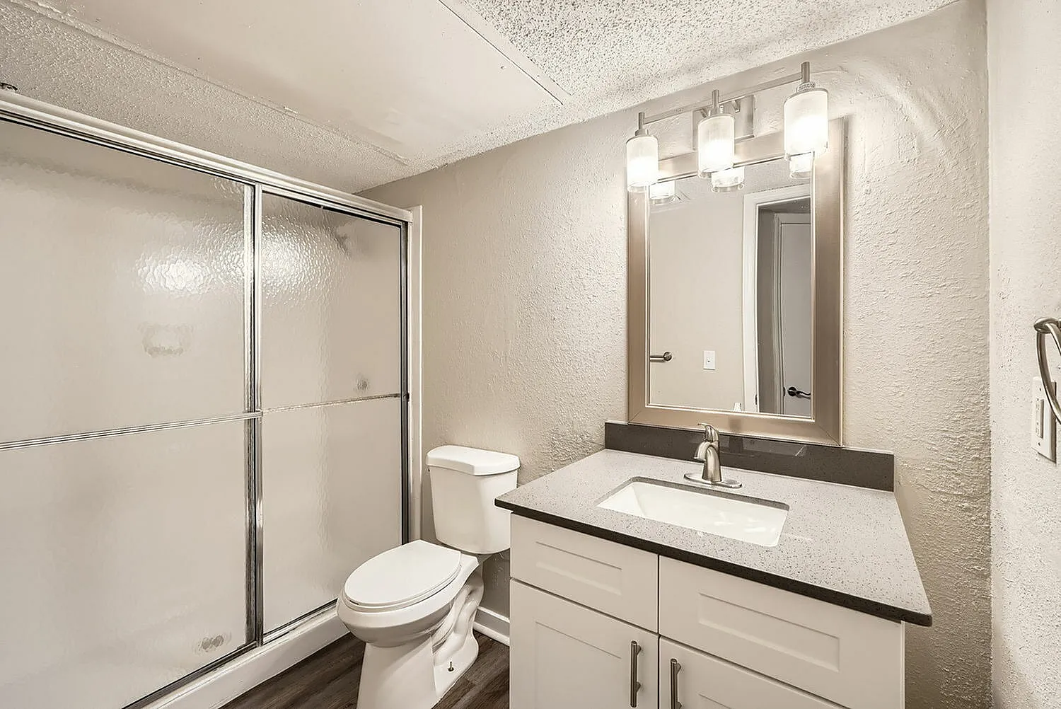 Primary bathroom, white vanity cabinetry, quartz countertops, framed mirror, glass shower enclosure