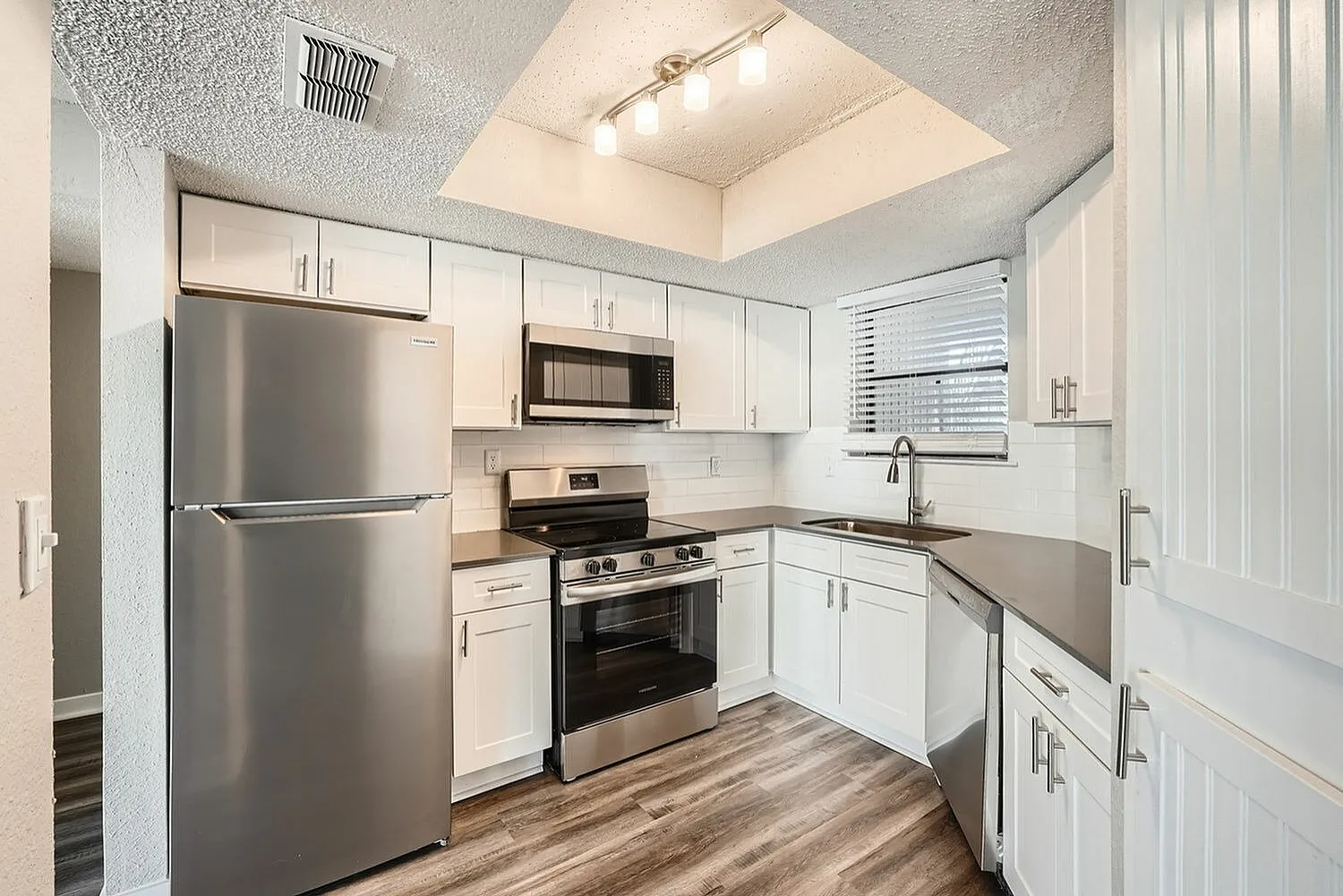 Kitchen, white shaker cabinetry, stainless appliances, gray quartz countertops, wood-style plank flooring, skylight