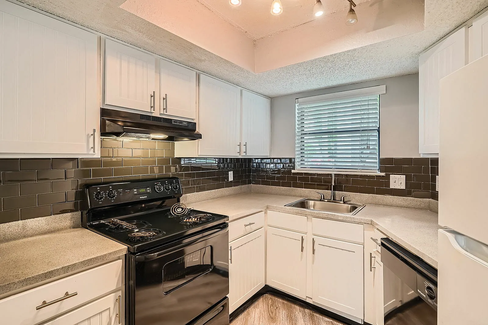 Kitchen, white shaker cabinetry, dark tile backsplash, black gas range, quartz countertops, wood-style plank flooring