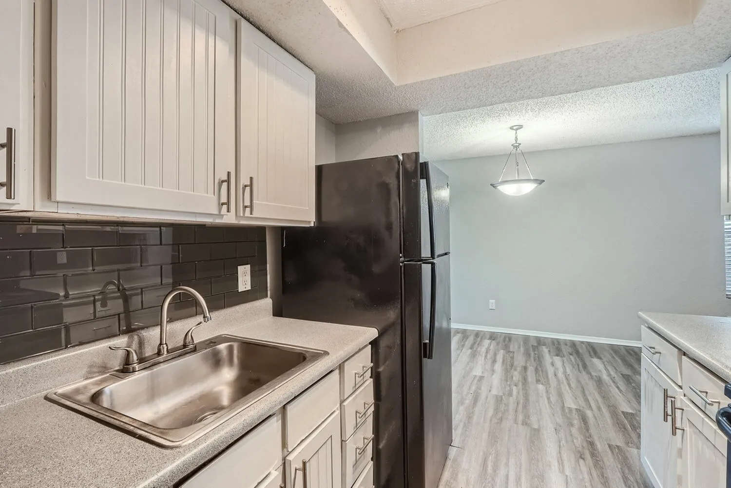 Kitchen, white shaker cabinetry, dark subway tile backsplash, stainless steel sink, black refrigerator