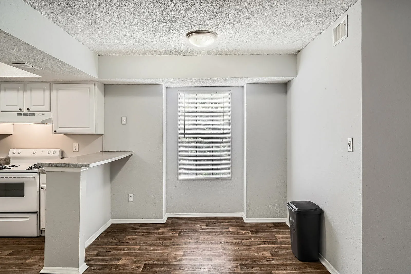 Kitchen with white cabinetry, stainless appliances, wood-style plank flooring, entry door with blinds