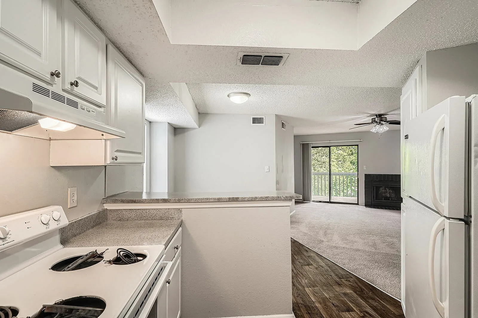 Kitchen with white shaker cabinetry, gray countertops, stainless appliances, wood-style plank flooring, open to living area with fireplace