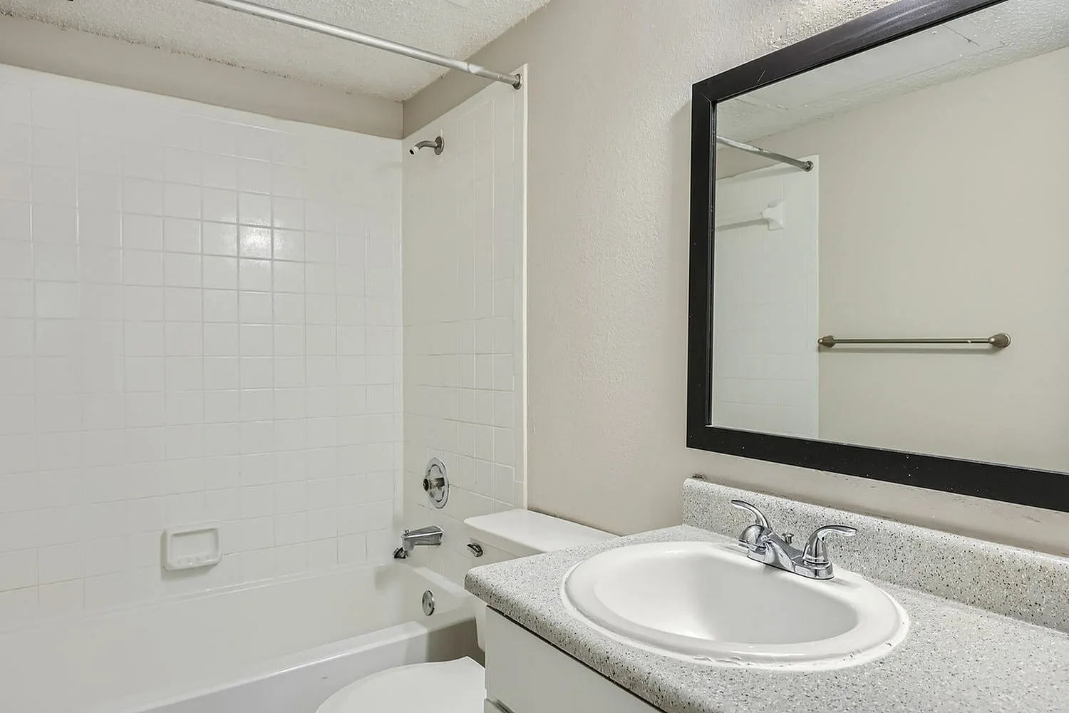 Bathroom, round white sink, gray speckled countertop, black framed mirror, white tile shower
