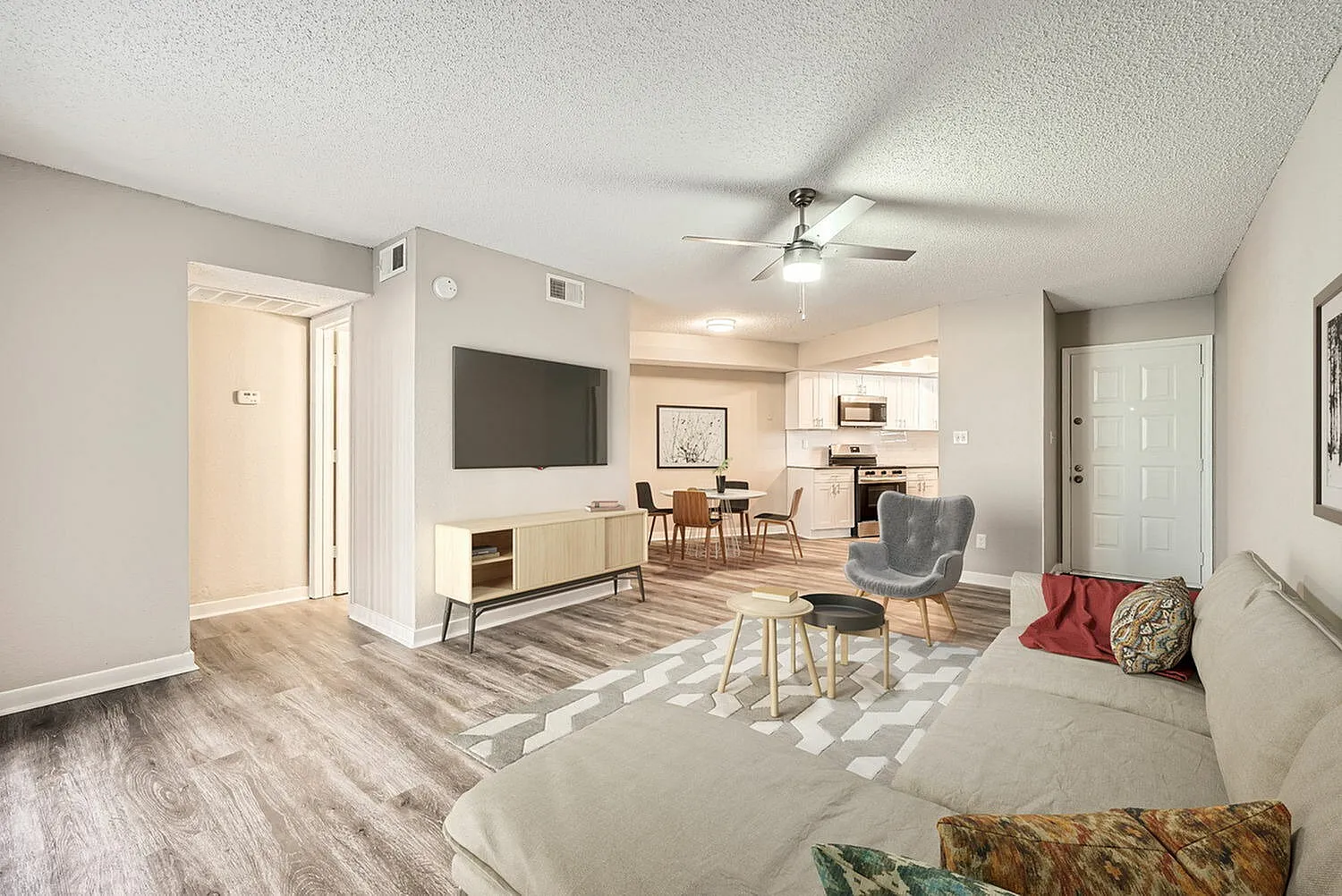 Living room and kitchen, wood-style plank flooring, wall-mounted TV, ceiling fan