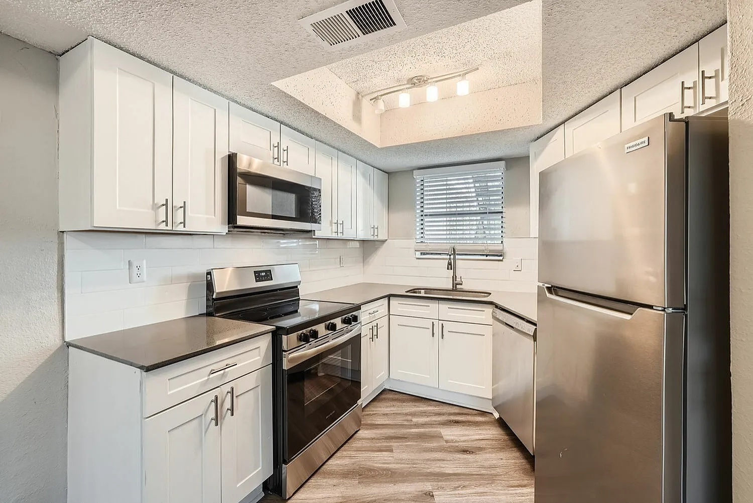 Kitchen, white shaker cabinetry, black countertops, stainless steel appliances, wood-style plank flooring