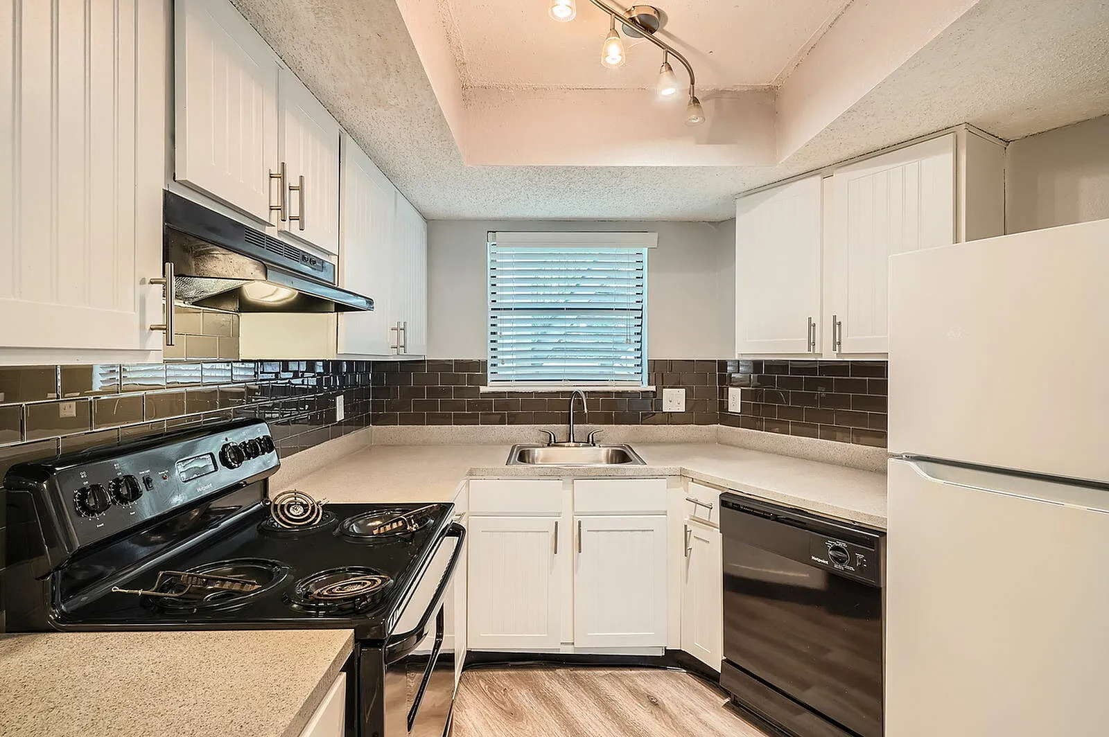 Kitchen, white shaker cabinetry, dark subway tile backsplash, stainless appliances, wood-style plank flooring