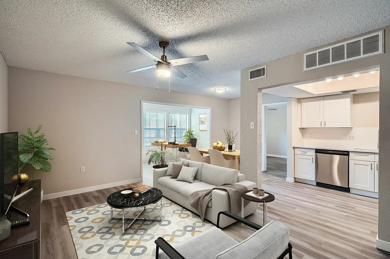 Living room with wood-style plank flooring, ceiling fan, sofa, kitchen with white cabinetry and stainless appliances