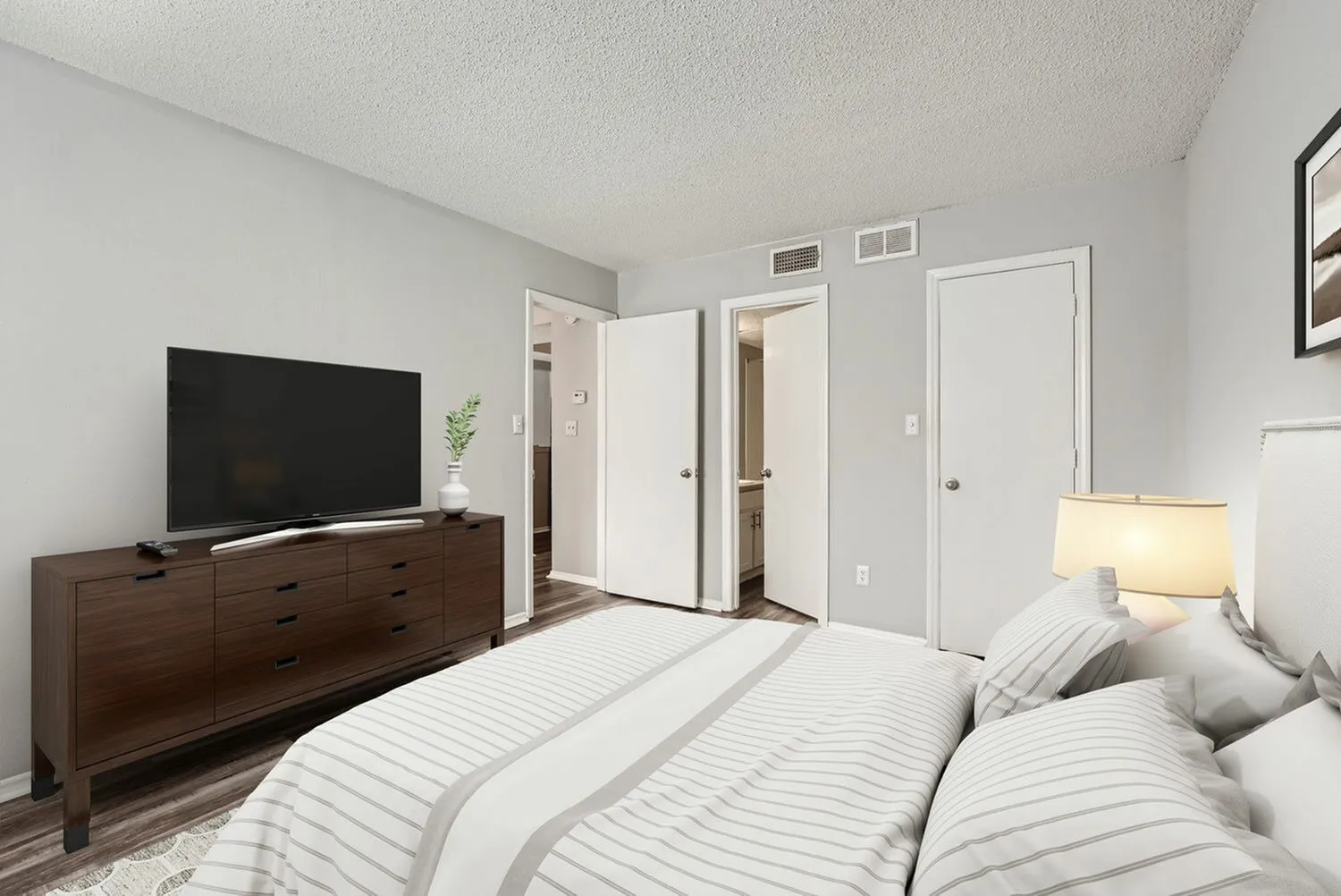 Primary bedroom, dark wood dresser with TV, striped bedding, wood-style plank flooring, white doors