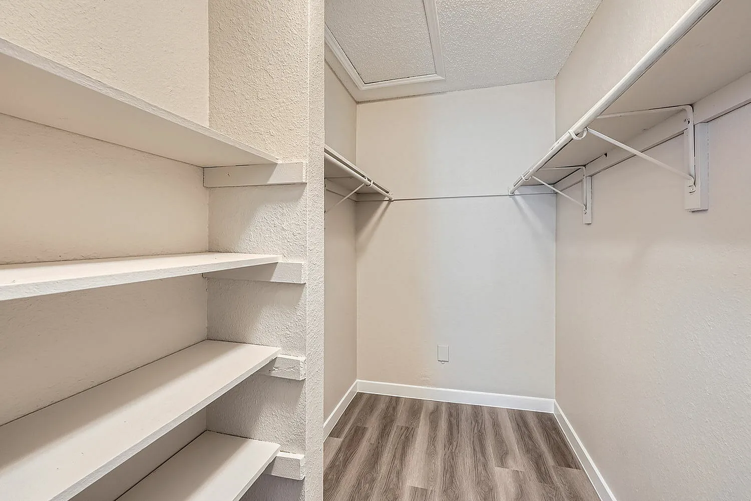 Walk-in closet, white shelving units, metal clothing rods, wood-style plank flooring