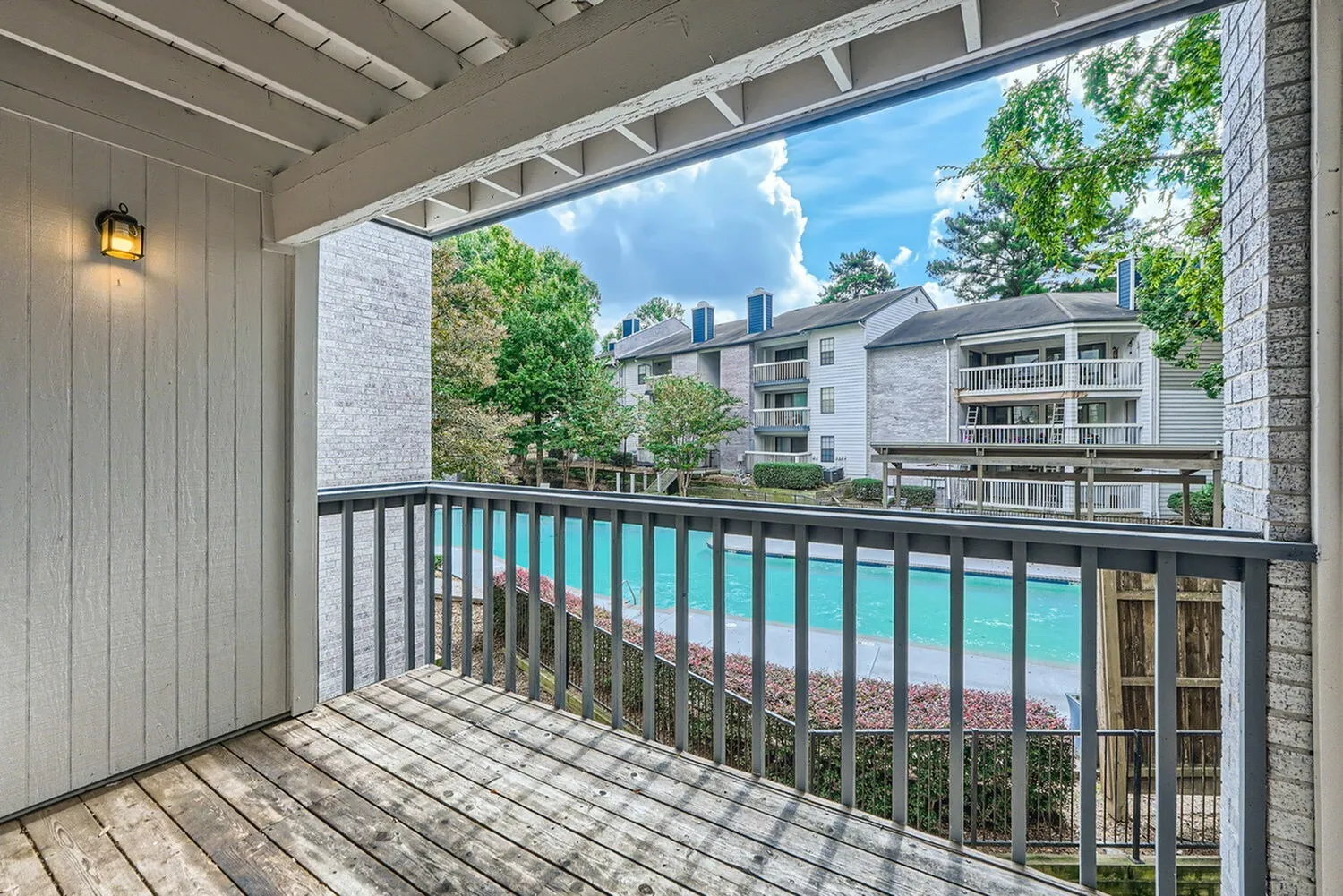 Covered balcony, wood-style plank flooring, black metal railing, turquoise pool view, landscaped grounds