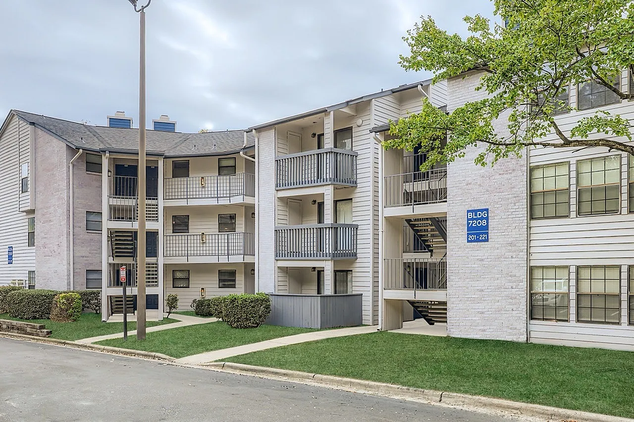 Multi-story residential complex, white and tan brick facade, balconies, manicured landscaping