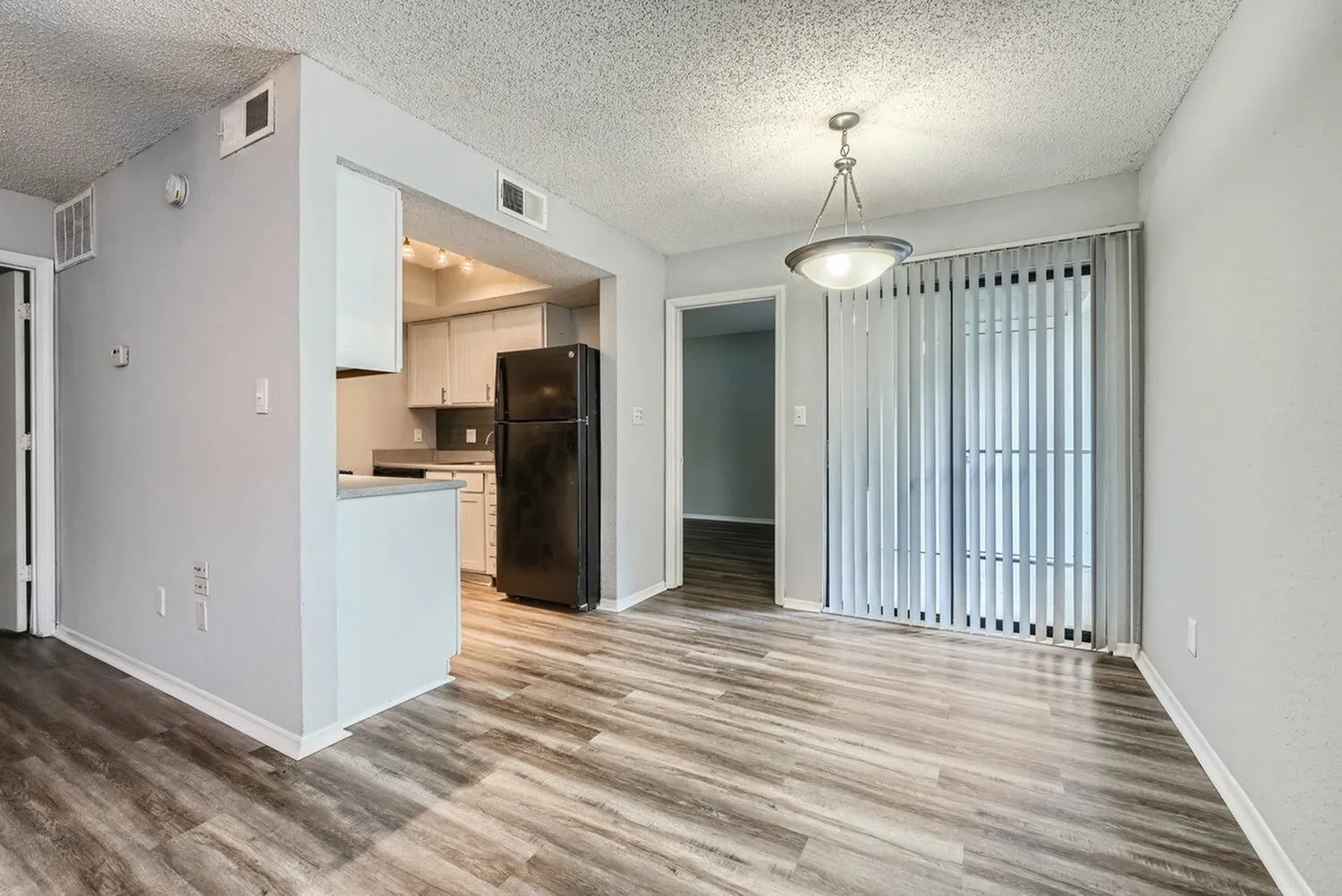 Living room and kitchen, wood-style plank flooring, white cabinetry, black refrigerator, pendant light