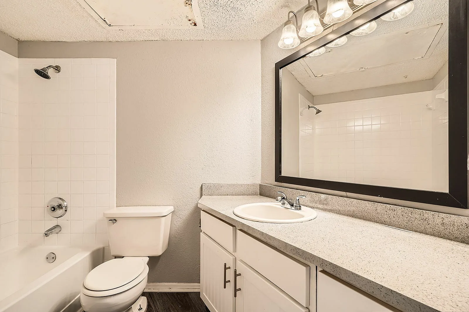 Bathroom, white cabinetry, quartz countertops, black-framed mirror, tile shower surround, dark wood-style plank flooring