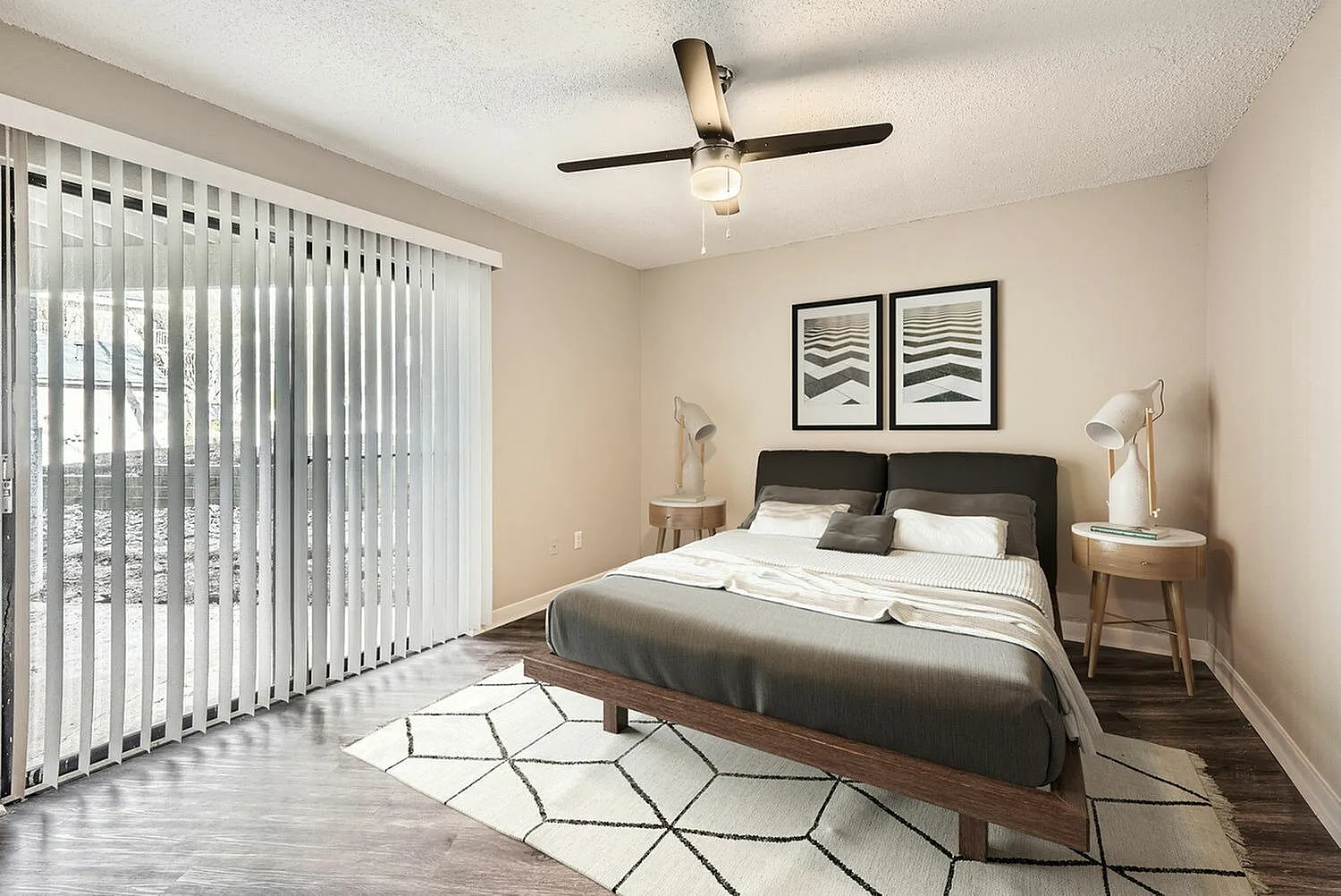 Primary bedroom, wood-style plank flooring, ceiling fan, dark upholstered bed, geometric area rug