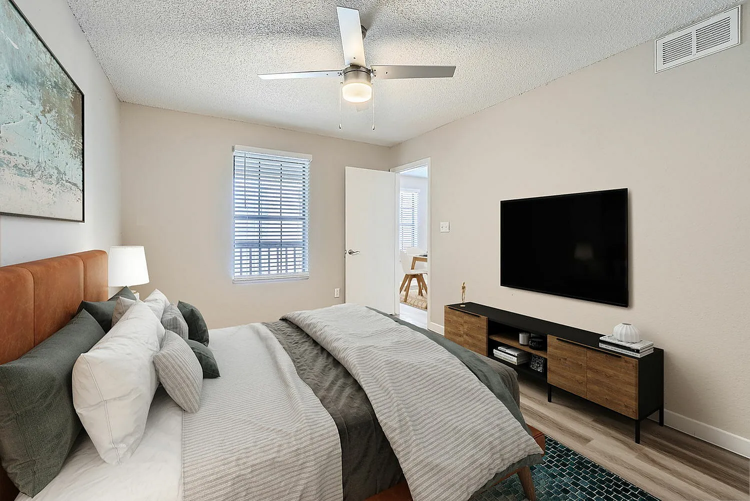 Primary bedroom, tan leather headboard, wood-style plank flooring, wall-mounted TV, ceiling fan