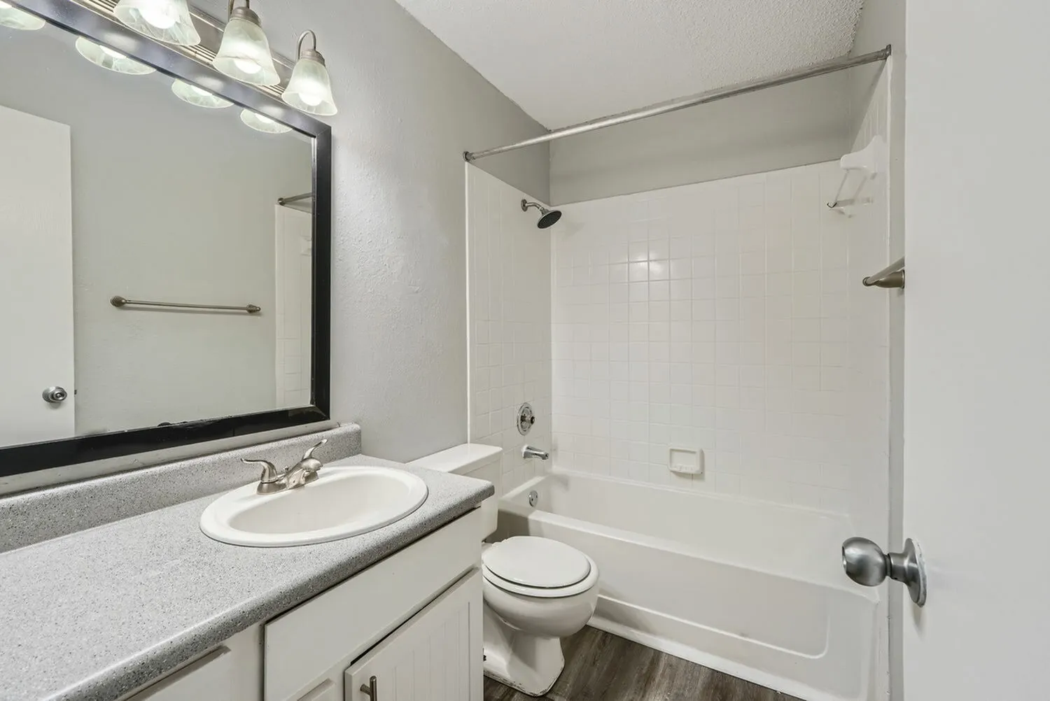 Bathroom, gray countertop, round white sink, framed mirror with lighting, toilet, tile shower enclosure