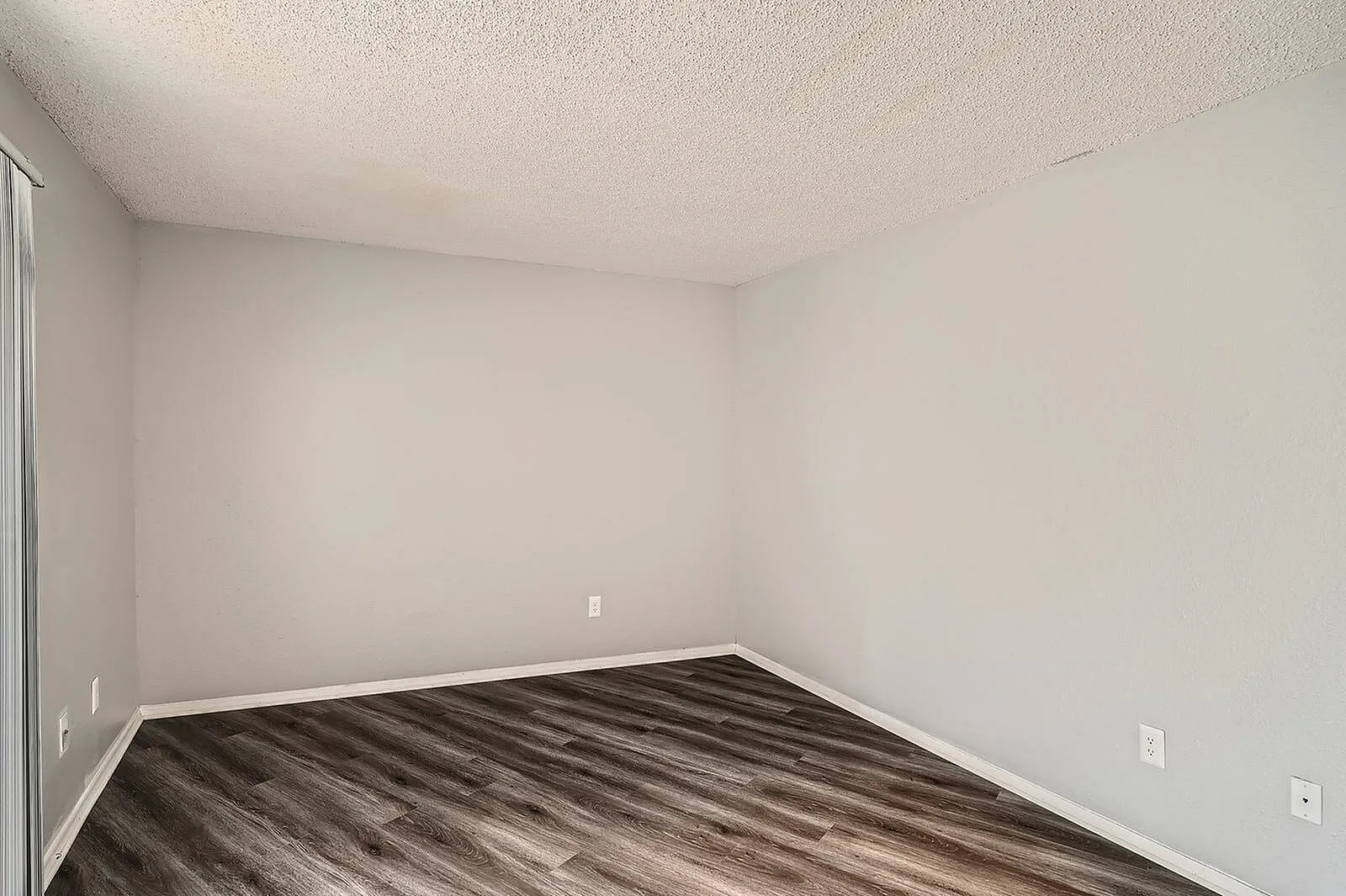 Bedroom, wood-style plank flooring, white walls, textured ceiling, wall outlets