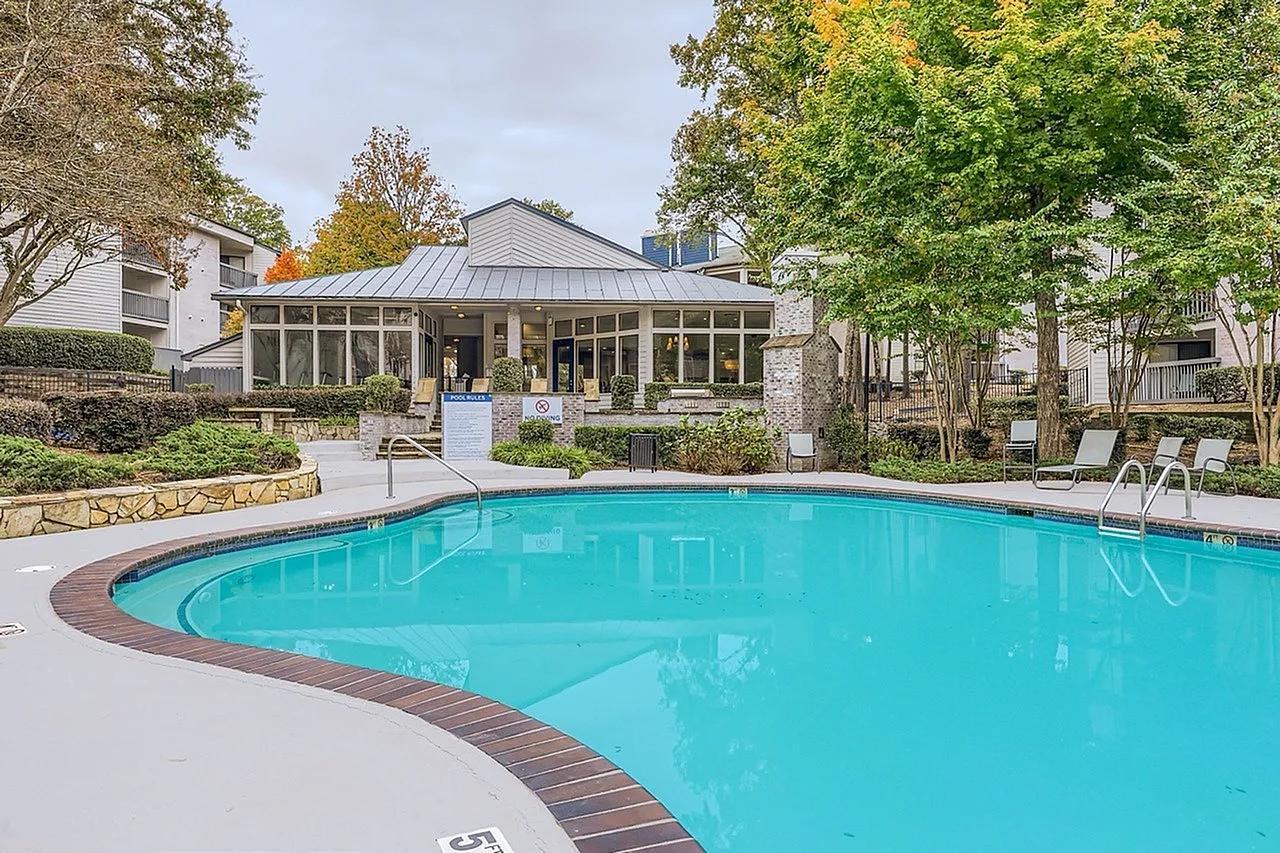Community pool area, turquoise water, curved dark deck border, covered pavilion with columns, lounge chairs