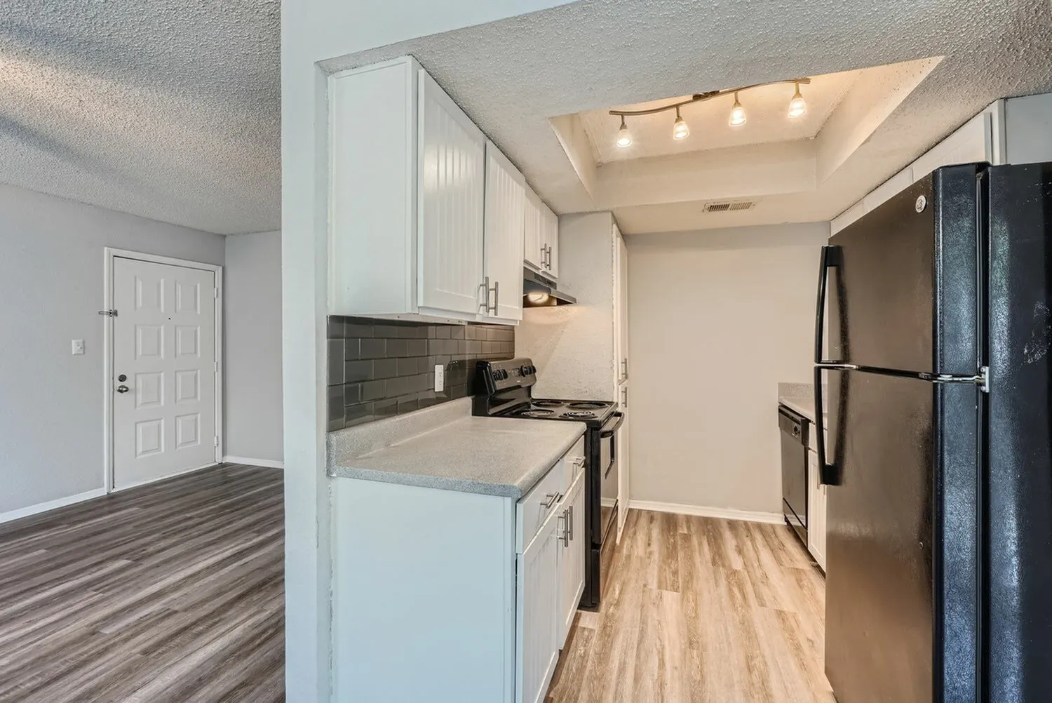 Kitchen with white shaker cabinetry, gray subway tile backsplash, stainless appliances, wood-style plank flooring, entry door visible