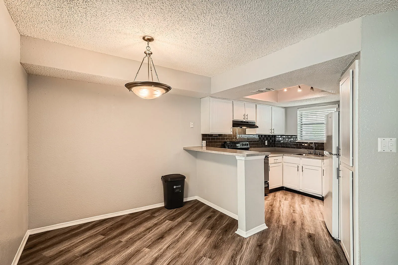 Kitchen, white shaker cabinetry, black countertops, stainless appliances, wood-style plank flooring