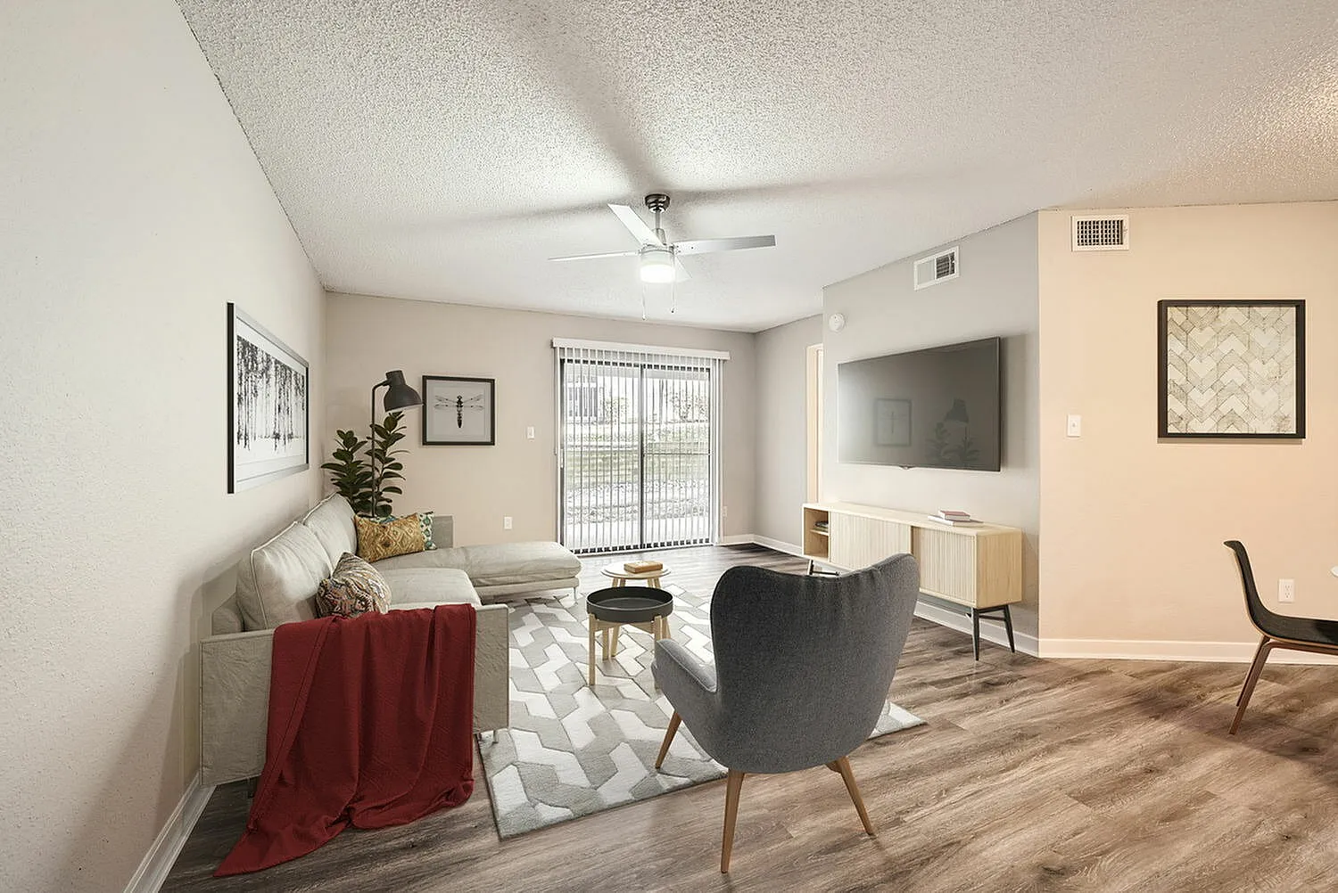 Living room with wood-style plank flooring, ceiling fan, gray upholstered armchair, geometric area rug, flat-screen TV