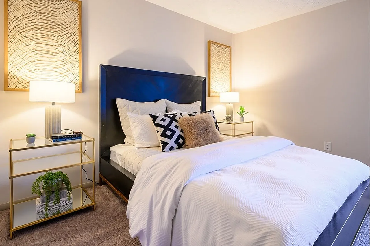 Primary bedroom, dark blue upholstered headboard, white bedding, wood-style plank flooring, brass nightstands